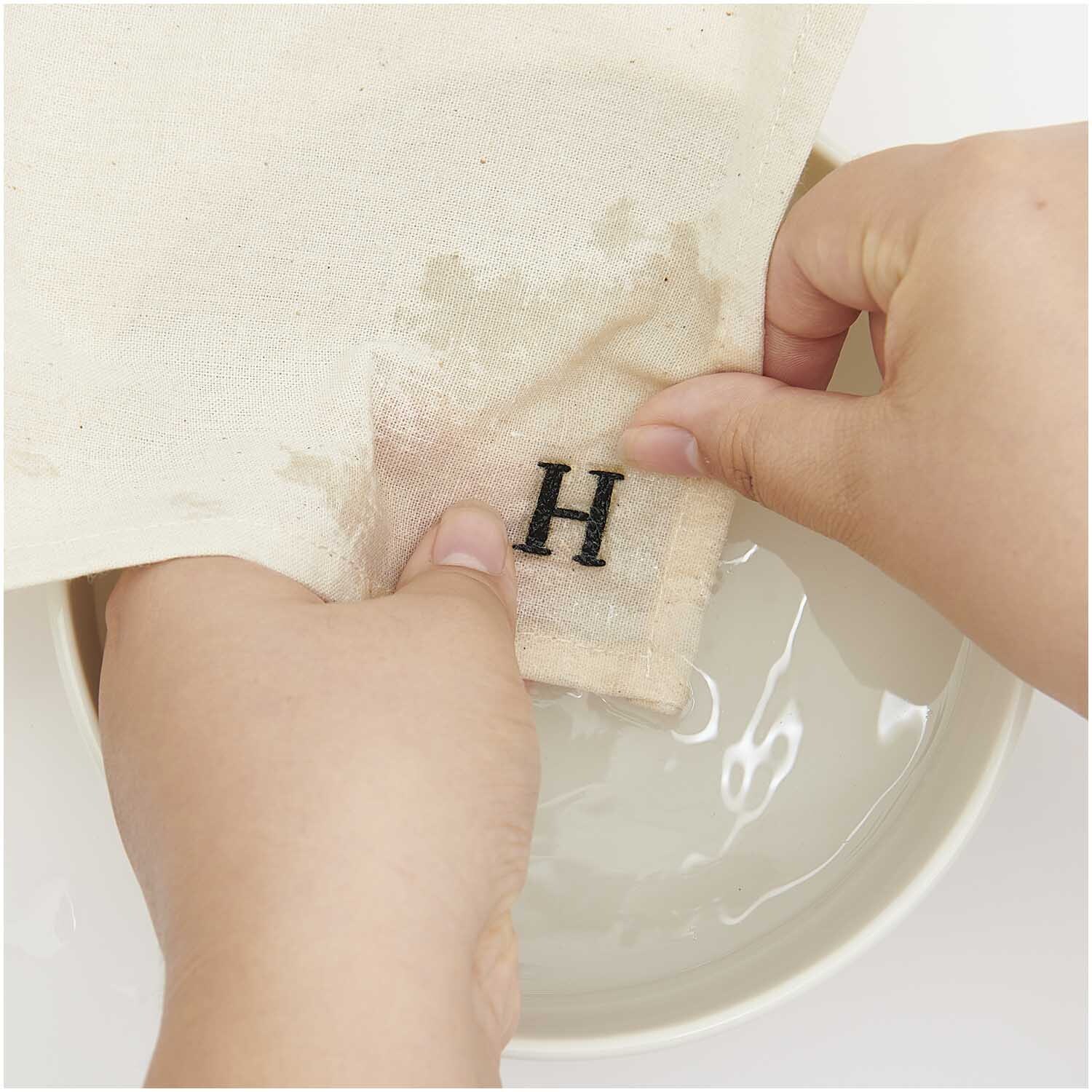 Stick and Stitch Stickpackung Alphabet zeigt Hände, die ein Tuch mit schwarzem Buchstaben "H" waschen.