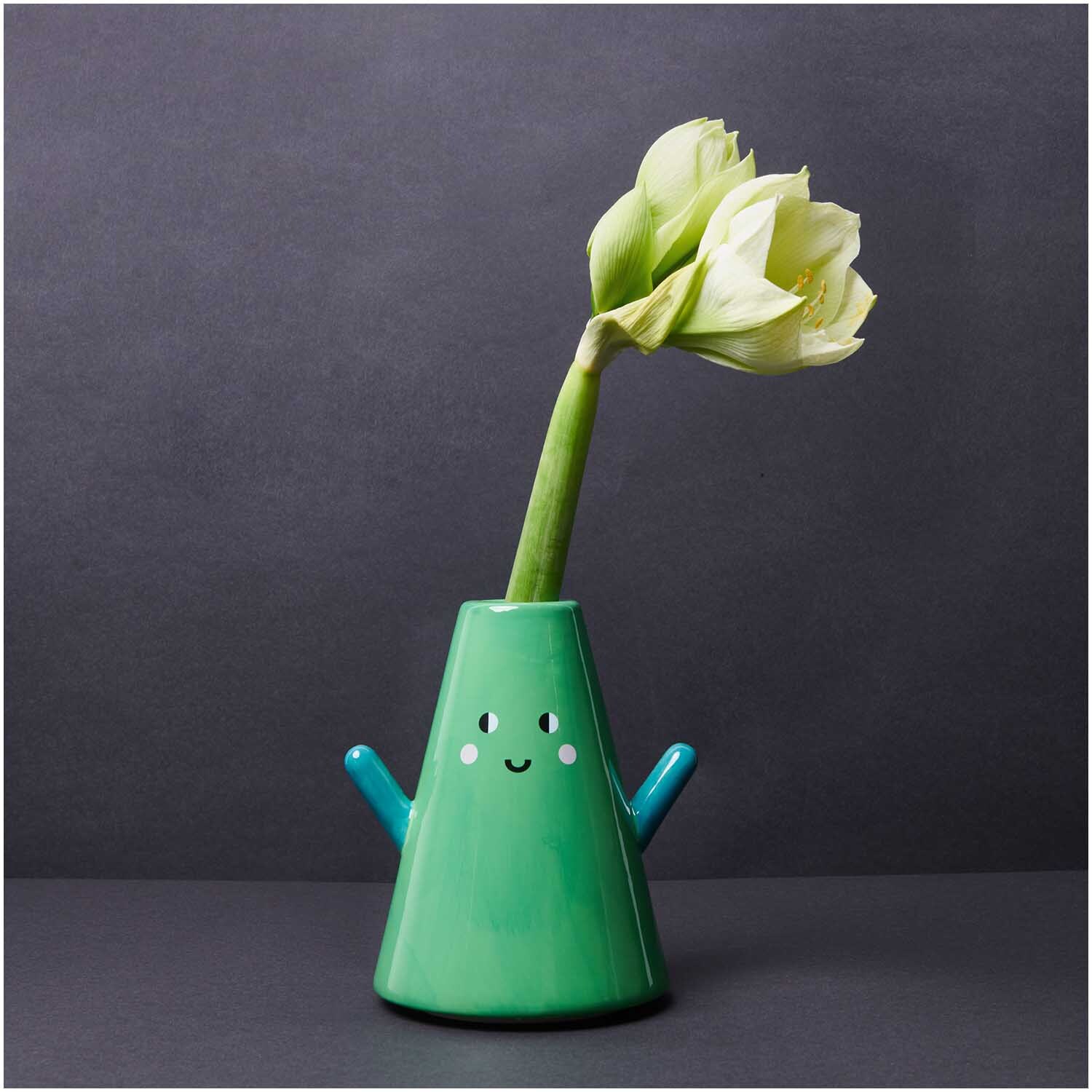 Keramik Vase Tanne grün 20cm: Fröhliche, grüne Vase mit Gesicht und Blumen auf dunklem Hintergrund.