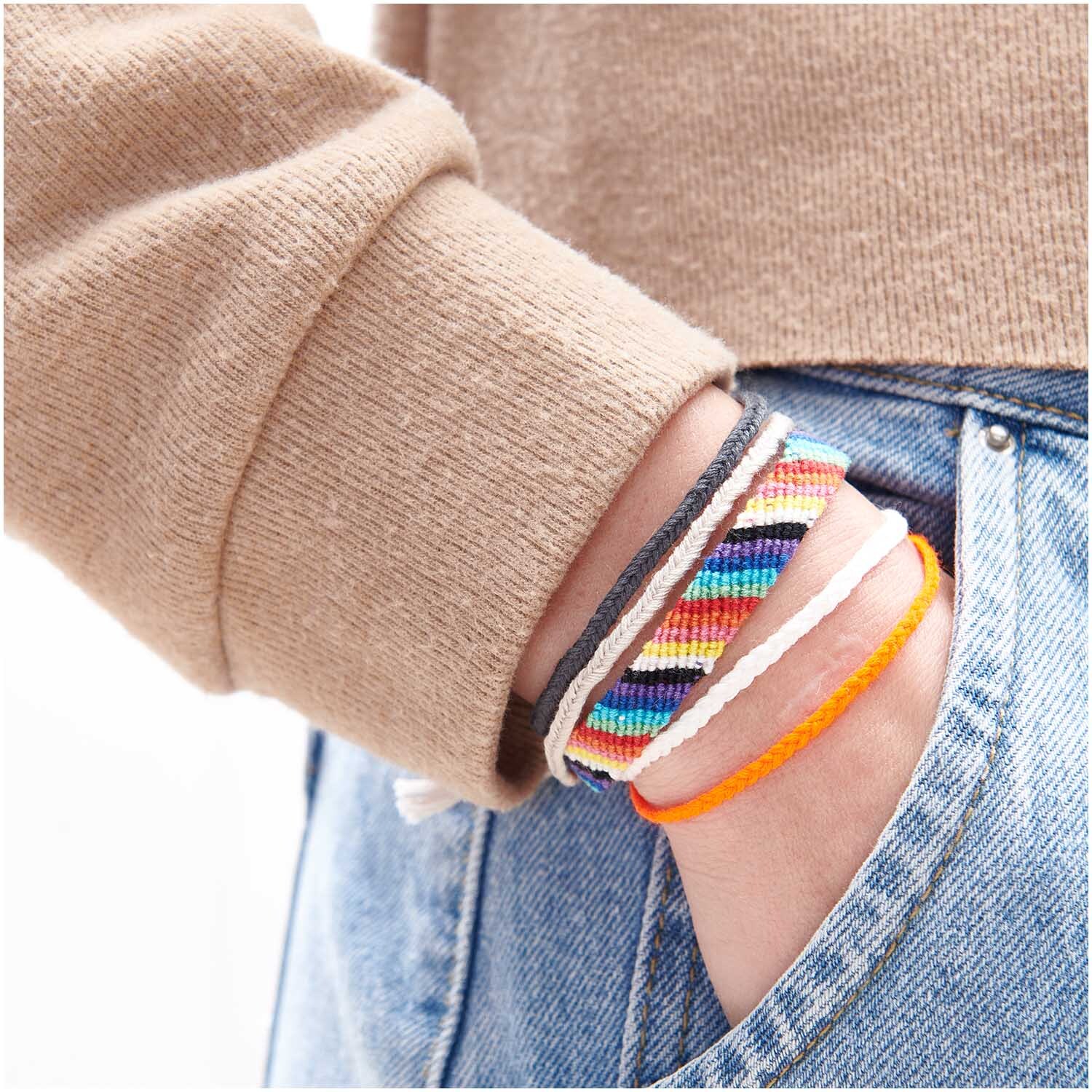 Stickgarn Set Multicolour Fashion: Handgelenk mit bunten Armbändern aus mehrfarbigem Garn von Rico Design, lässig in Hosentasche gesteckt.