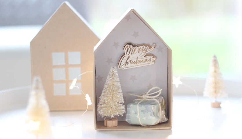 Bastelanleitung Geldgeschenk in Weihnachtskulisse: Miniaturhaus mit Tannenbaum und Geschenk.