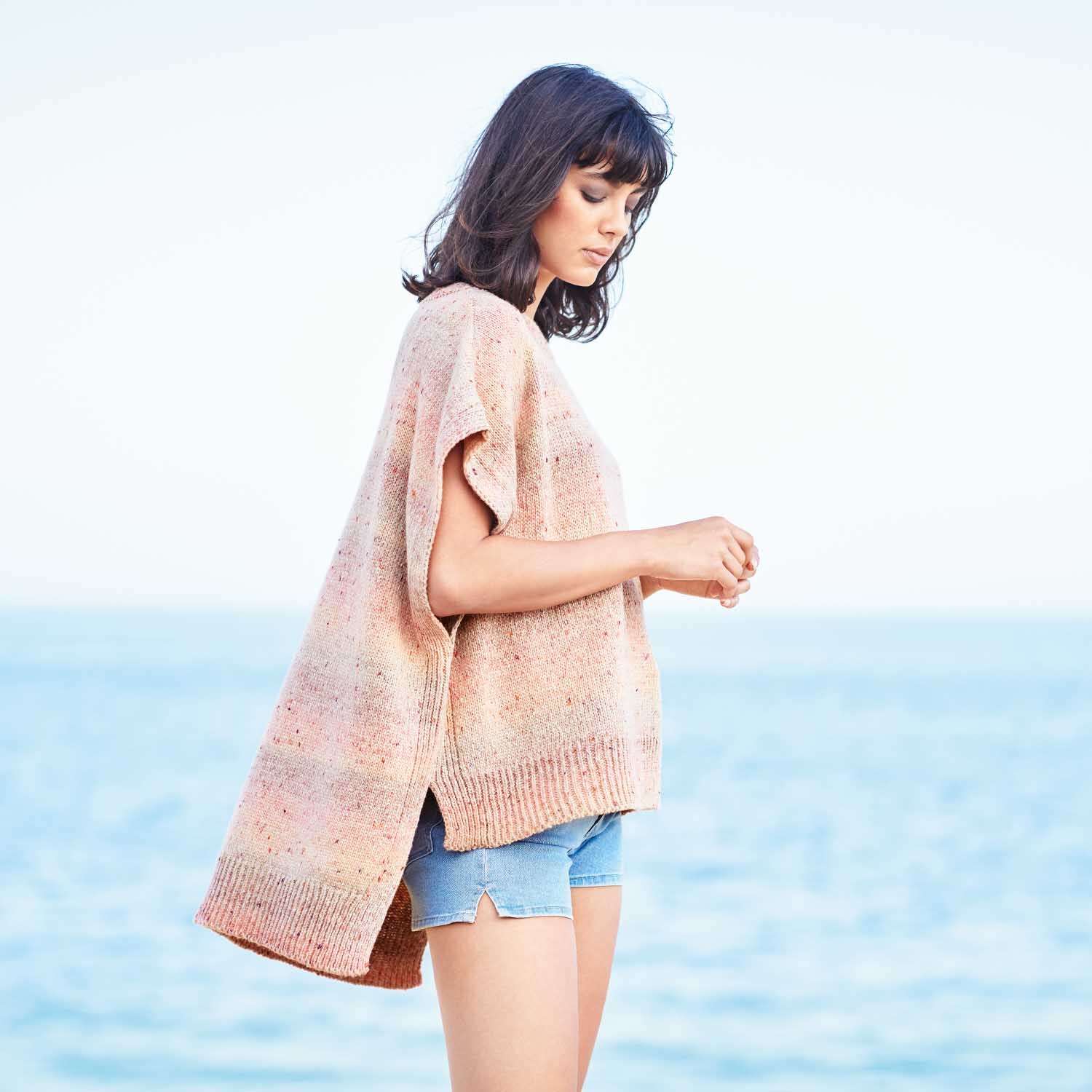 Strickanleitung Shirt aus Fashion Cotton Light & Long Tweed dk: Frau am Strand in lockerem, pastellfarbenem Strickshirt und Jeansshorts.