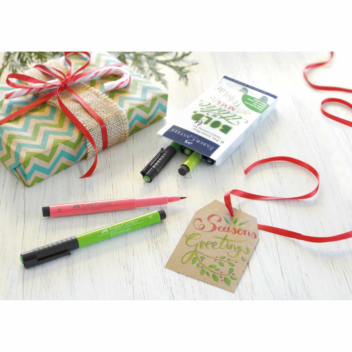 Tuschestift Pitt Artist Pen Handlettering Grüntöne 6 Stück von Faber Castell neben Geschenk und Karte auf Holztisch.