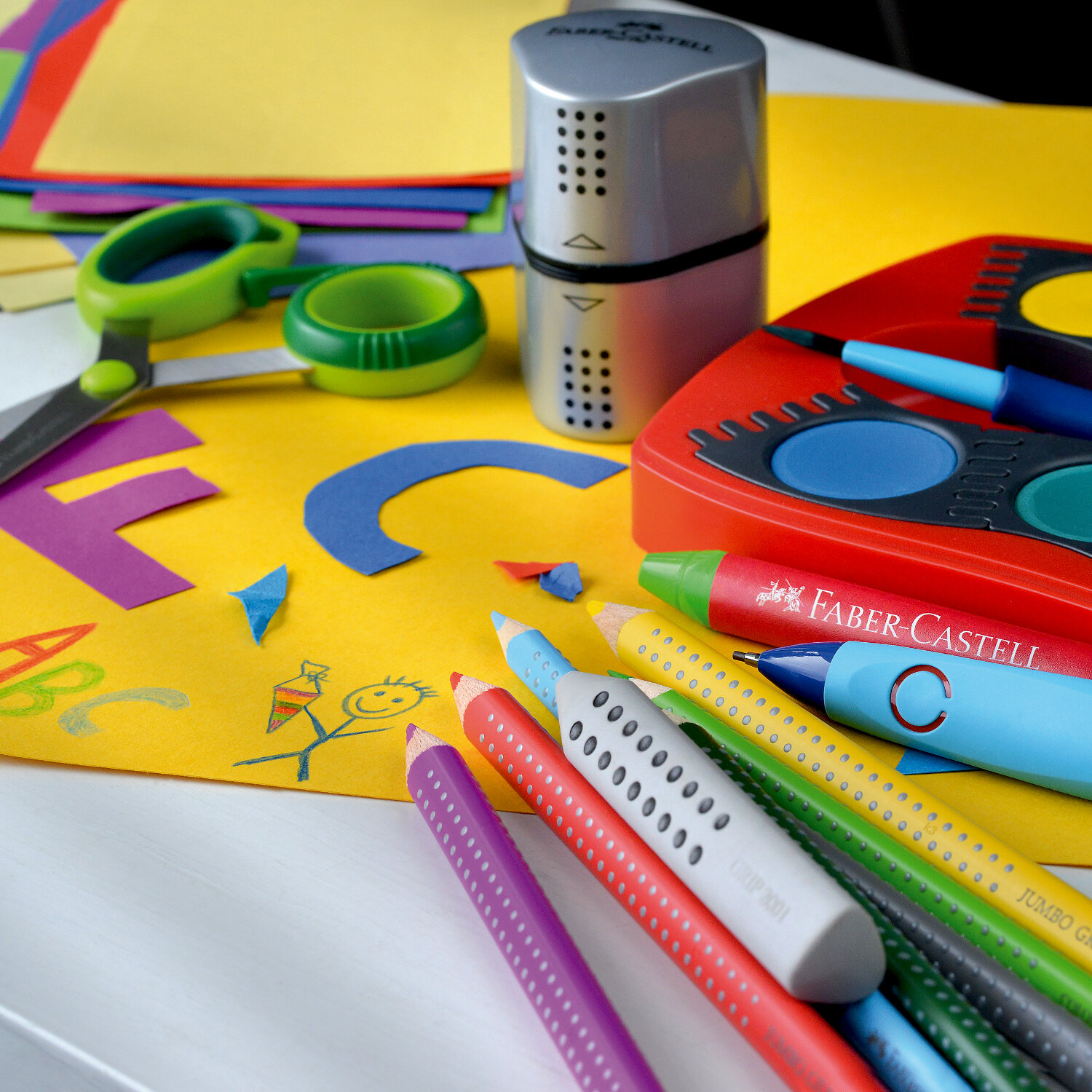 Colour Grip 2001 Stifte von Faber Castell auf einem Tisch mit buntem Papier und Bastelzubehör.