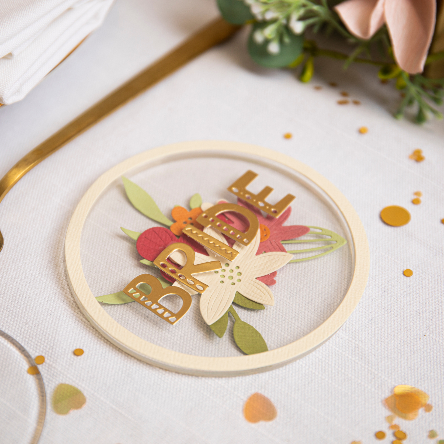 Framelits Die Set Circle Frames 6PK zeigt einen dekorativen Kreisrahmen mit Blumen und dem Wort "BRIDE" in Gold auf einem Tisch.