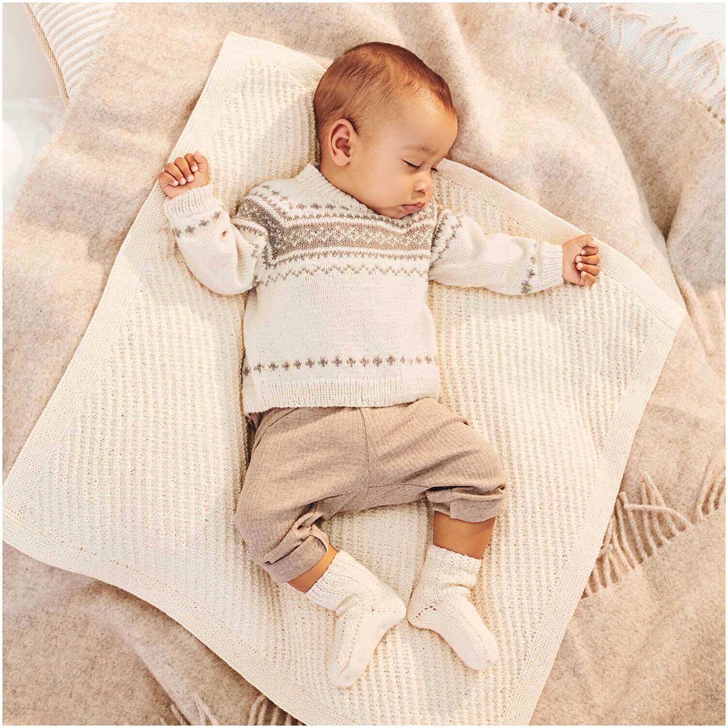 Baby Merino: Ein Baby schläft friedlich auf einer cremefarbenen Decke, gekleidet in einem gestrickten Pullover von Rico Design.