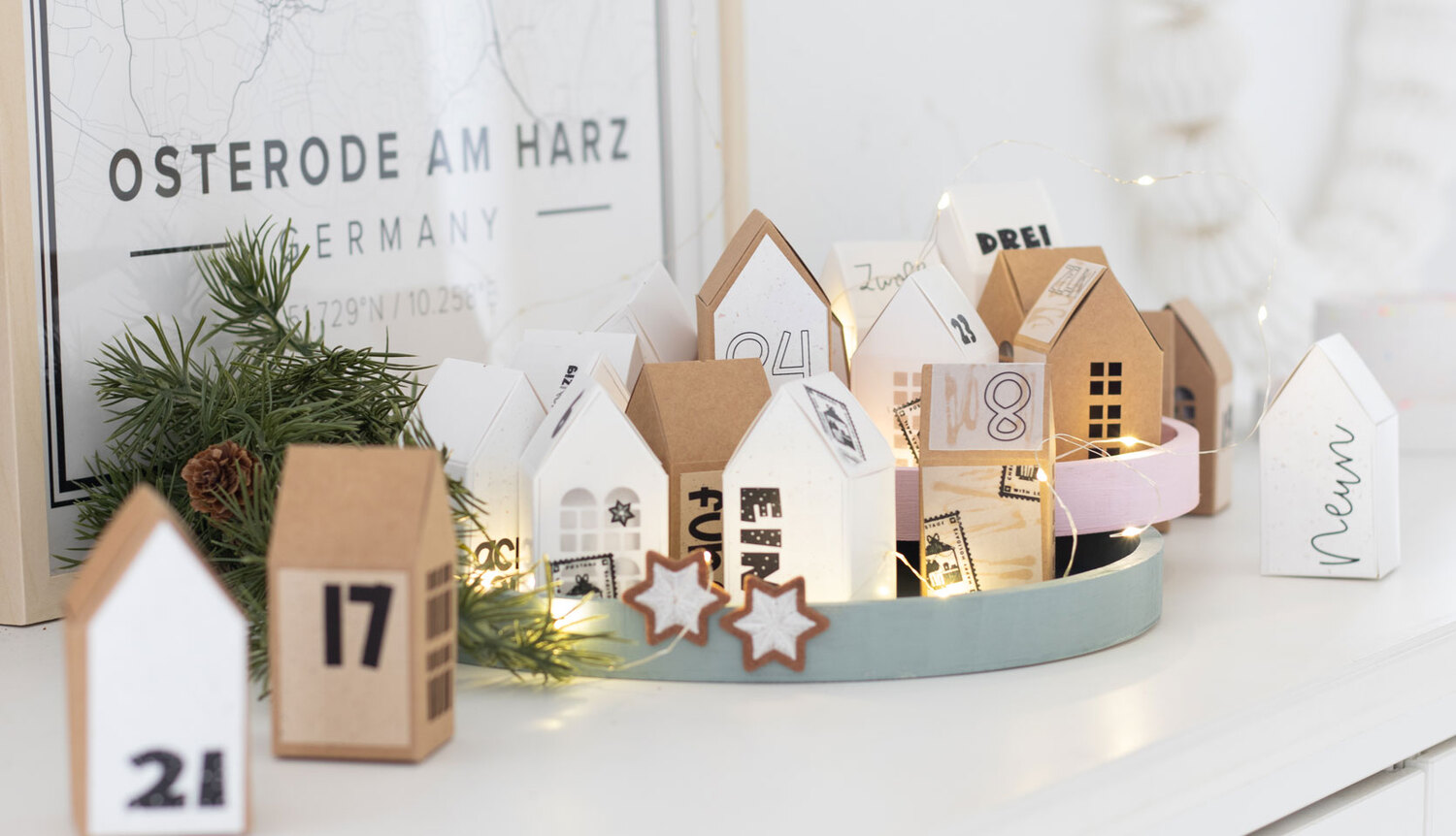 Inspiration Adventskalender Weihnachtsdorf @machsschoen: Dekoratives Dorf aus Papphäusern in Weiß und Braun auf einem Tablett mit Lichtern.