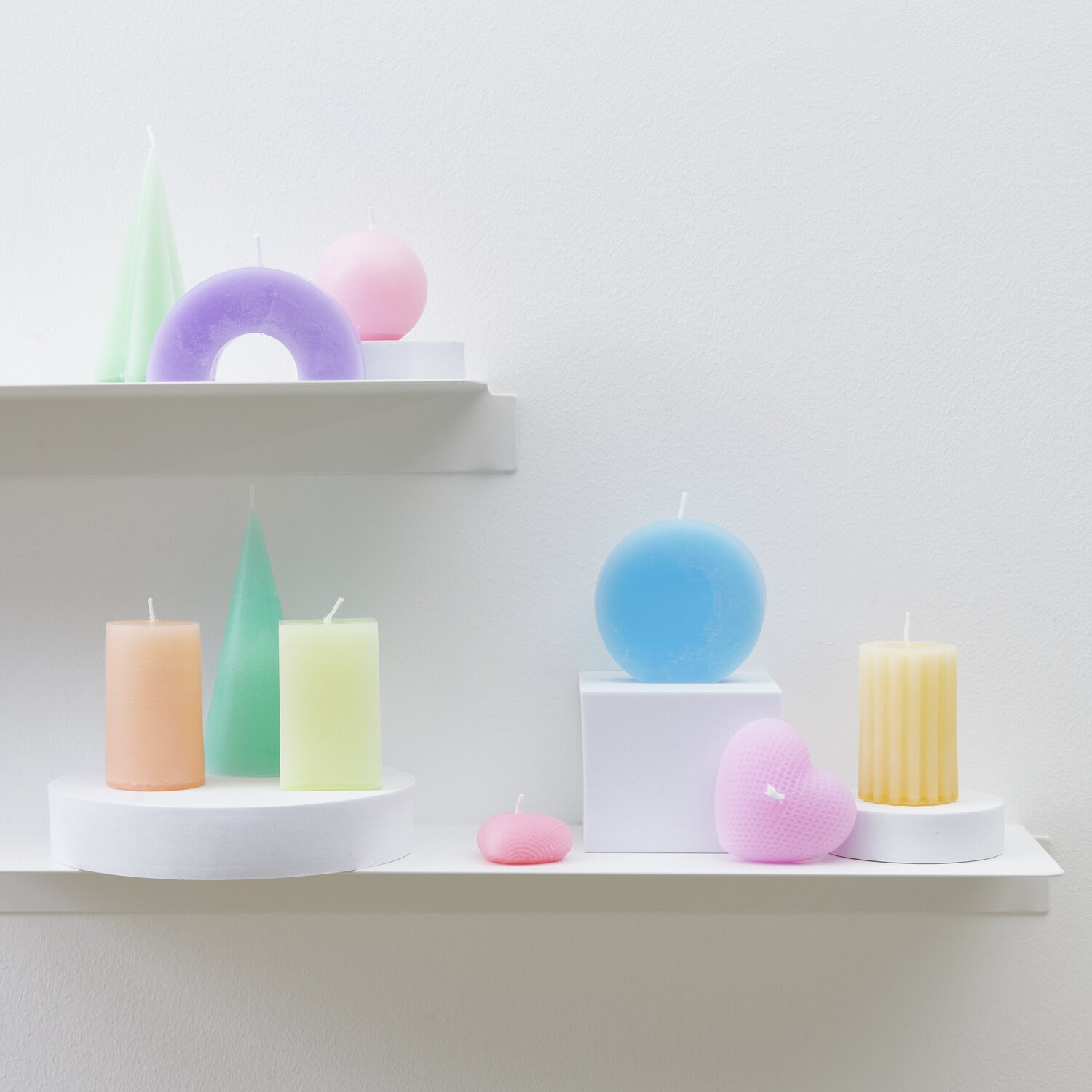 Kerzenwachs Granulat: Bunte Kerzen in Pastellfarben auf weißen Regalen, ideal für kreative Dekorationen.