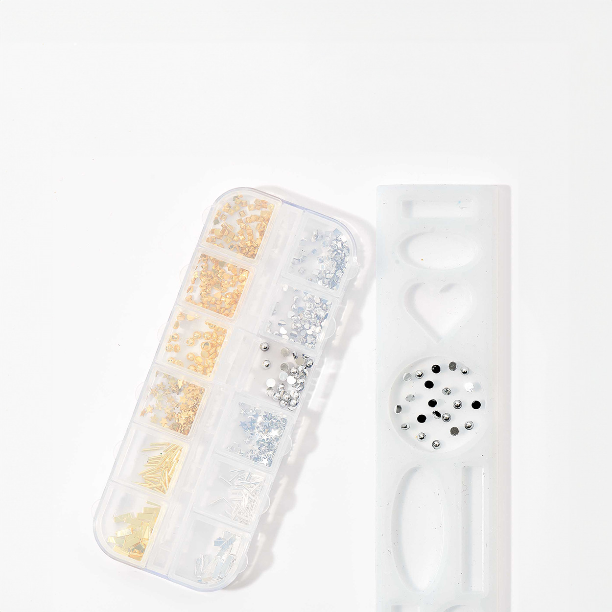 Eine Sortierbox mit golden und silbernem Füllmaterial, sowie eine Silikonform mit silbernem Füllmaterial ausgelegt.
