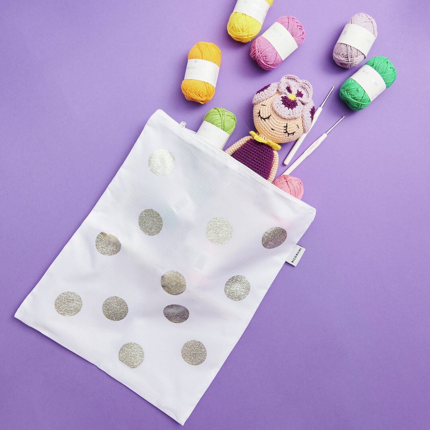 Creative Bag Ricorumi in 30x38cm mit silbernen Punkten, gefüllt mit bunten Garnen und einer gehäkelten Puppe auf lila Hintergrund.