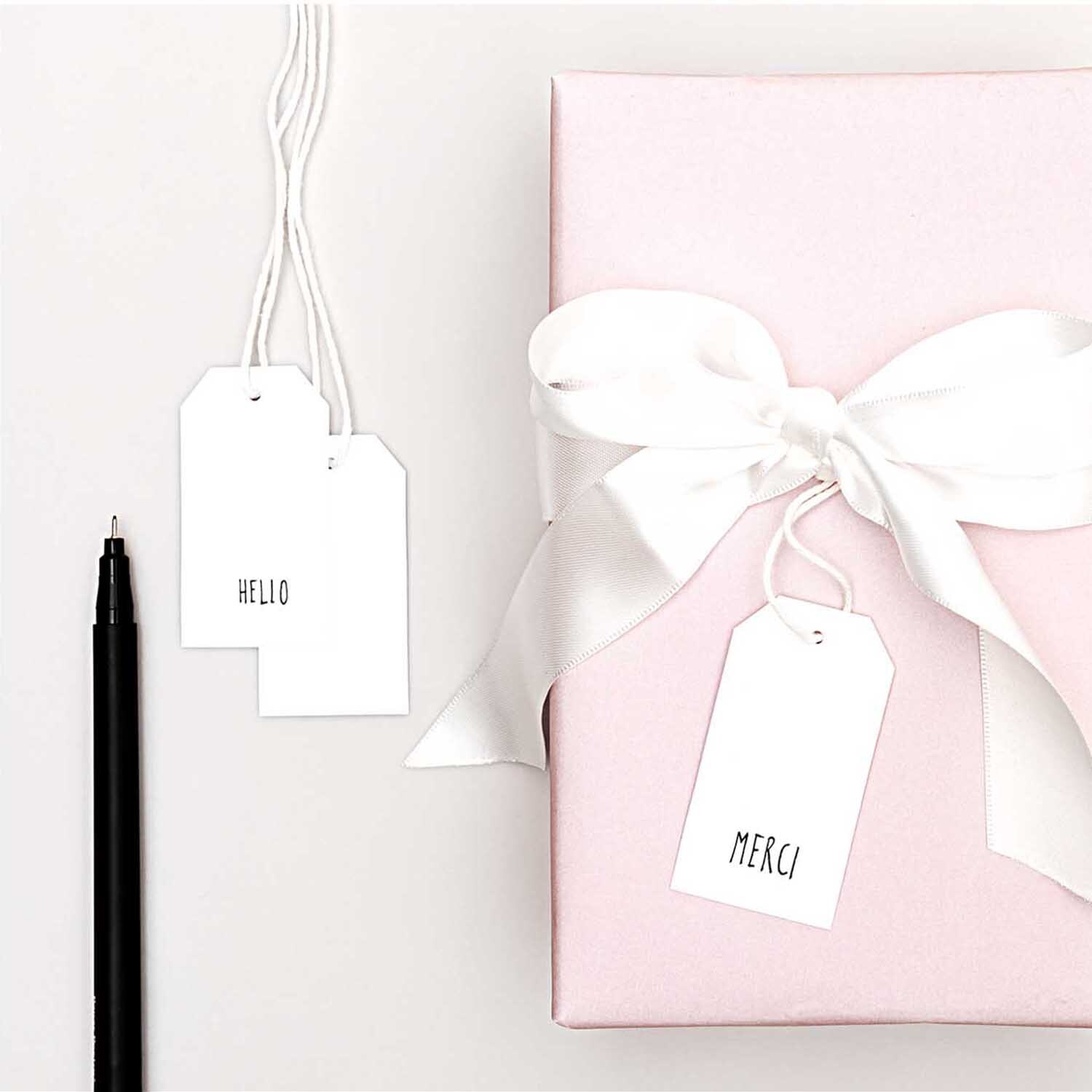 Paper Poetry Papieranhänger weiß 24 Stück neben rosa Geschenk mit weißer Schleife und schwarzem Stift.