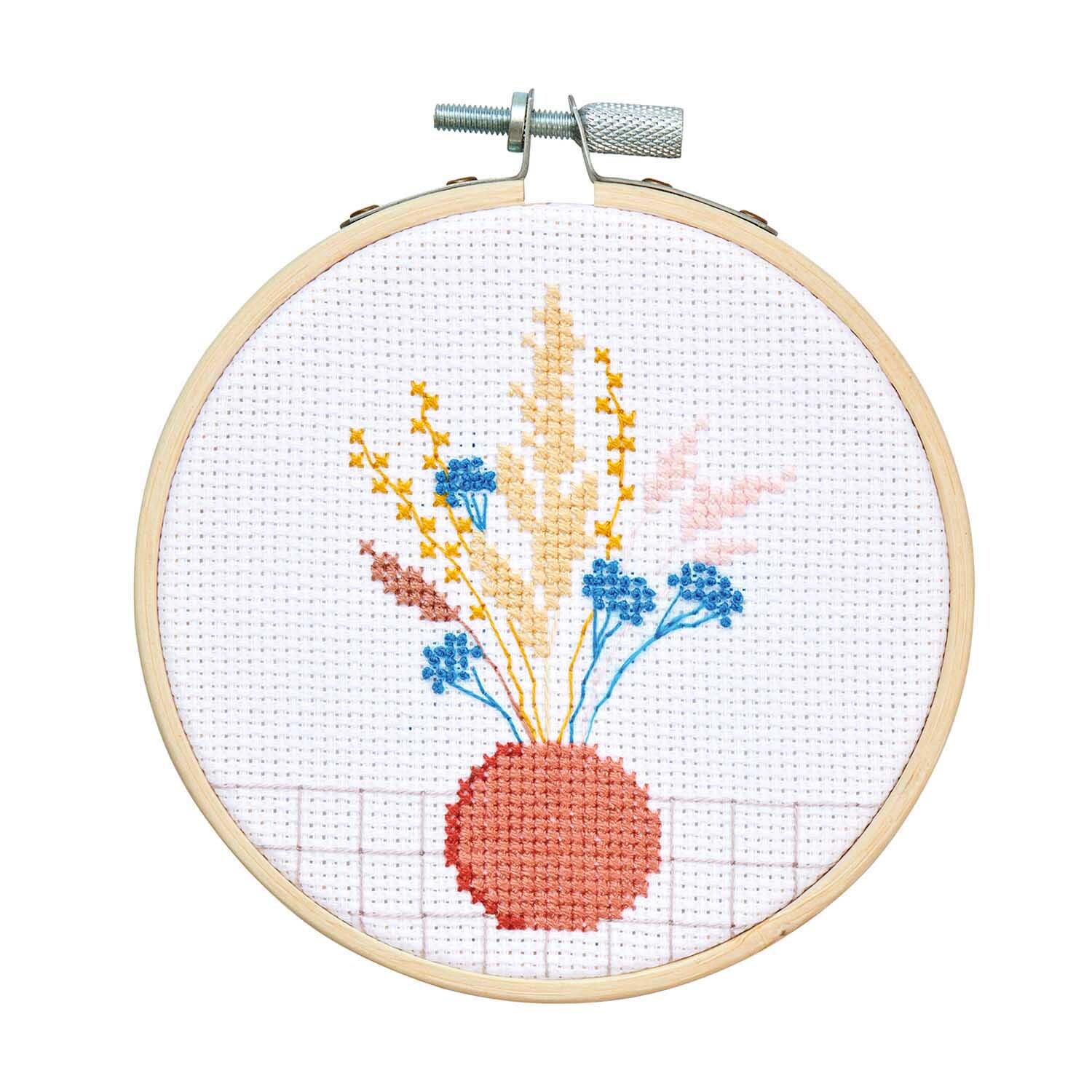Stickpackung Mini Kit Trockenblumen Bild Ø 10cm zeigt bunte Blumen in roter Vase, umrahmt von einem Holzstickrahmen.