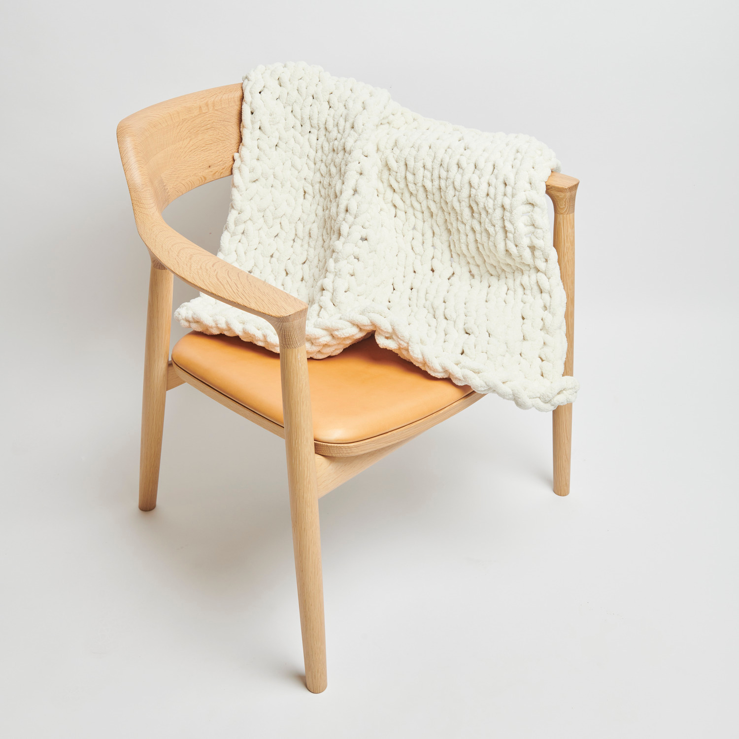 Chenillove Super Big: Cremefarbene Strickdecke von Rico Design auf einem Holzstuhl drapiert.