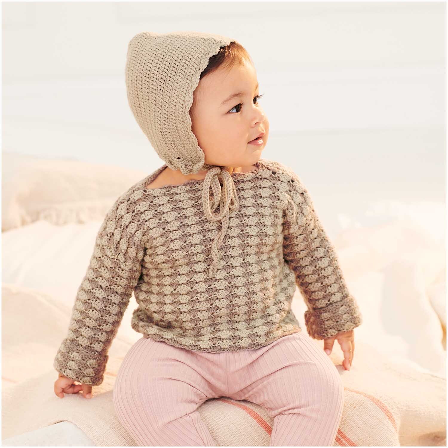 Baby Merino: Ein Baby trägt einen gestrickten Pullover und eine Mütze in Naturtönen, von Rico Design.