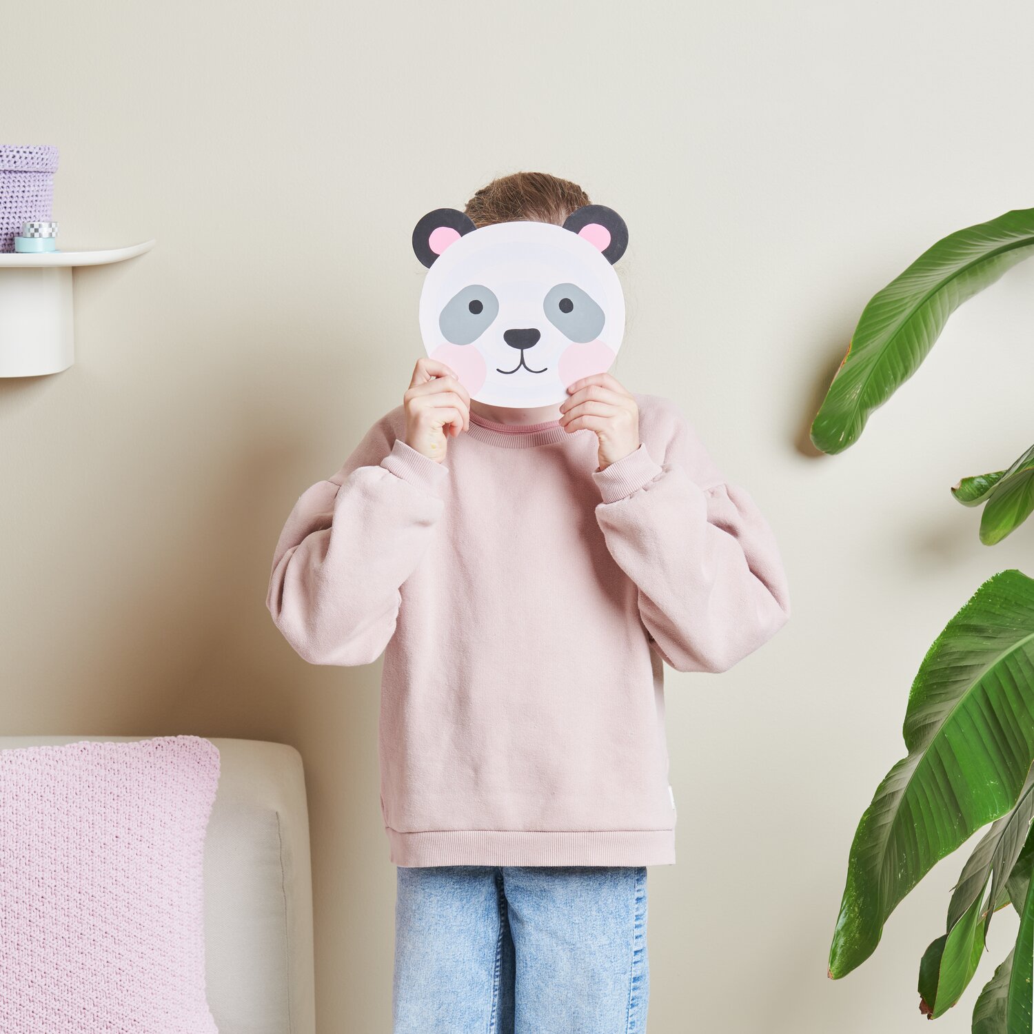 Malen nach Zahlen Panda: Person hält Panda-Maske vor Gesicht, trägt rosa Pullover, umgeben von Pflanzen.
