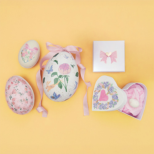 Ostereier zum befüllen, sowie Schachteln in unterschiedlichen Formen mit Blumenmuster und Schleife verziert. Flatlay von Produkten.