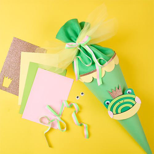 Schultüte mit Froschdesign und passendes Bastelpapier. Flatlay von Produkten.