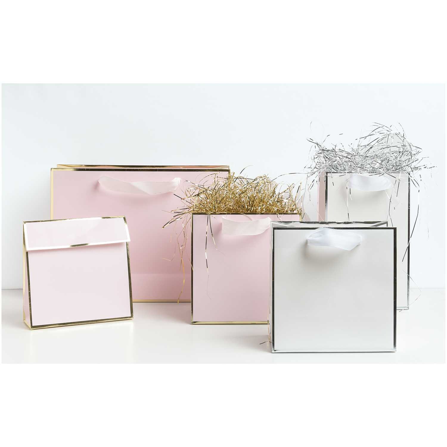 Paper Poetry Geschenktasche in elegantem Design, umgeben von weiteren Taschen in Rosa und Weiß. Ideal für stilvolle Geschenke.