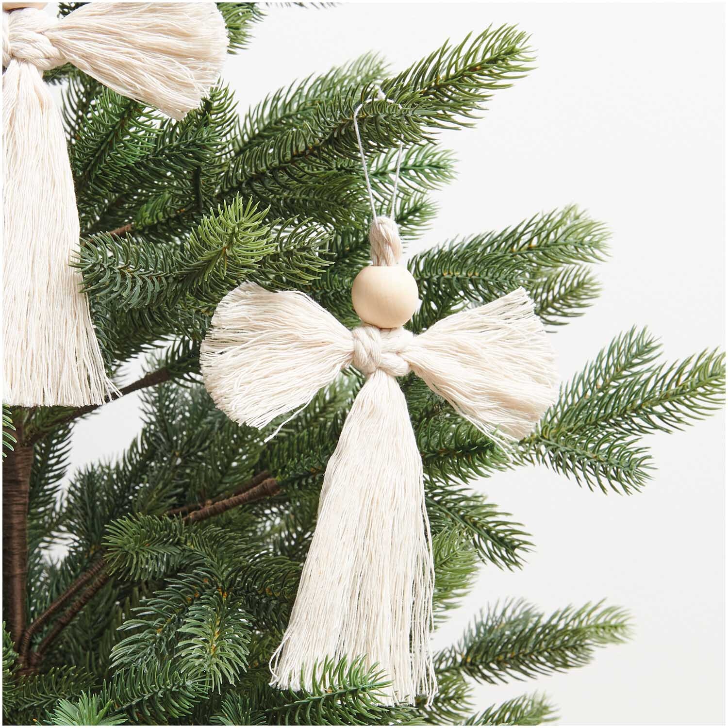 Makramee Set Engel 3 Stück 15x13cm: Handgefertigter Engel aus beigem Garn, hängend an einem grünen Tannenbaum.