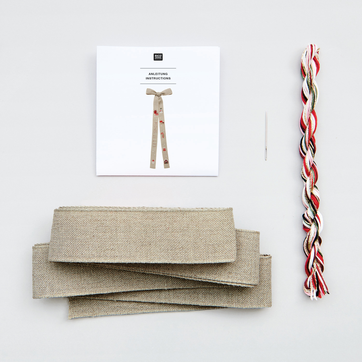 Stickpackung Schleife Let it Snow zeigt eine Anleitung, Stoffstreifen und Garn in natürlichen Tönen. Ideal für kreative Projekte.
