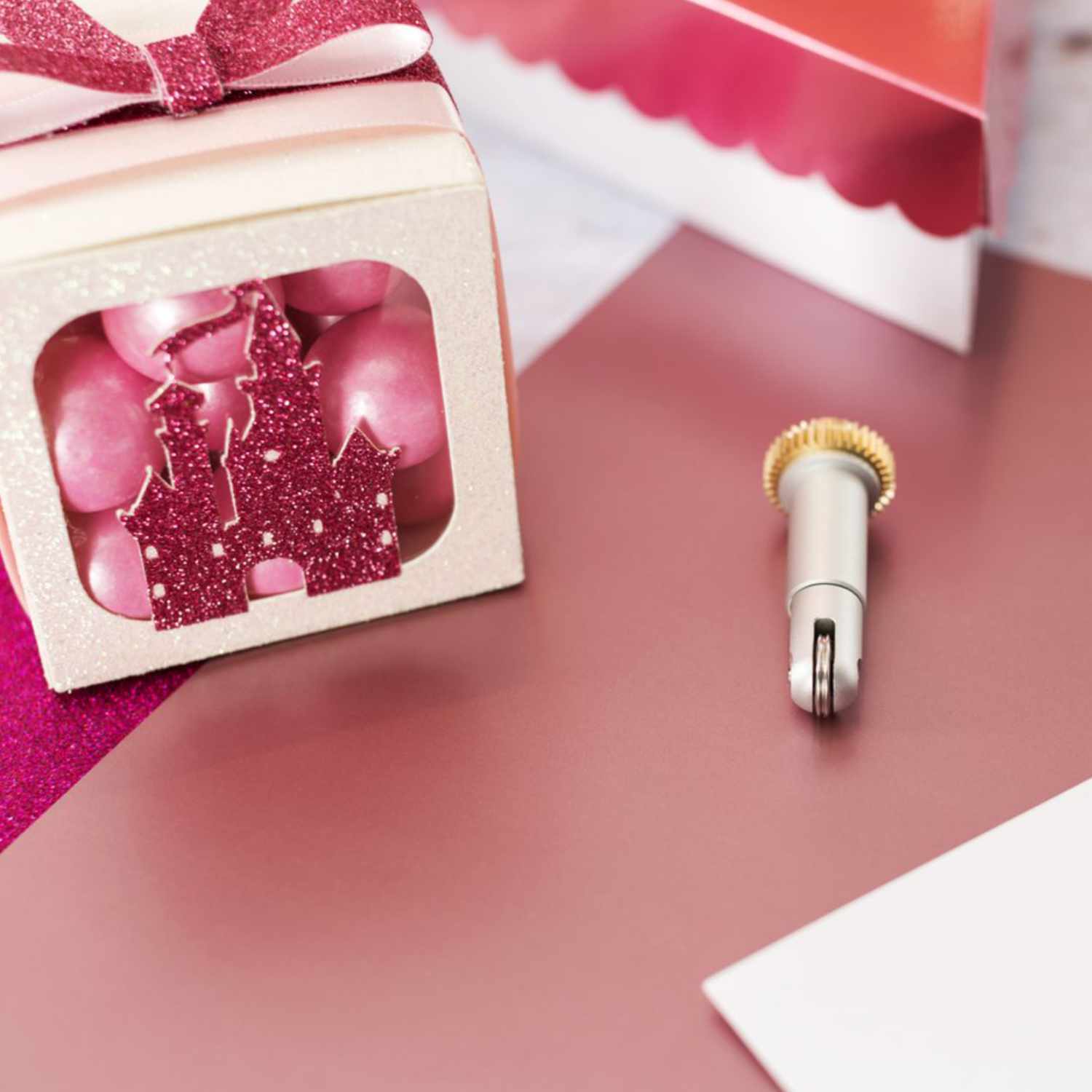 Maker Double Scoring Wheel Tip 02 neben einer Geschenkbox mit rosa Glitzerdekor auf rosa Papier.