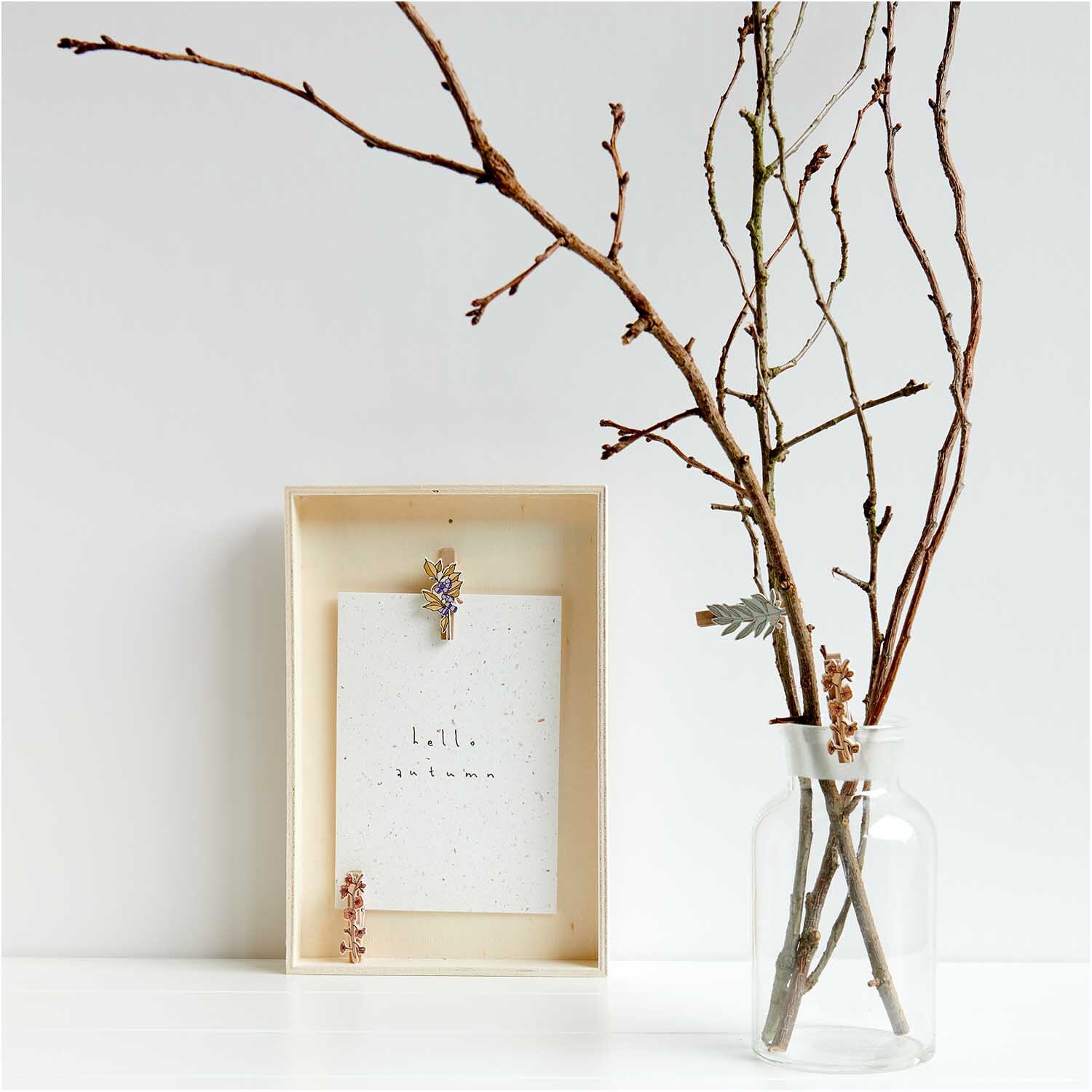 Holzclips Blumen Mix bunt 4,8cm 4 Stück: Mehrfarbige Clips von Rico Design an einem Holzrahmen, daneben ein Glas mit Zweigen.