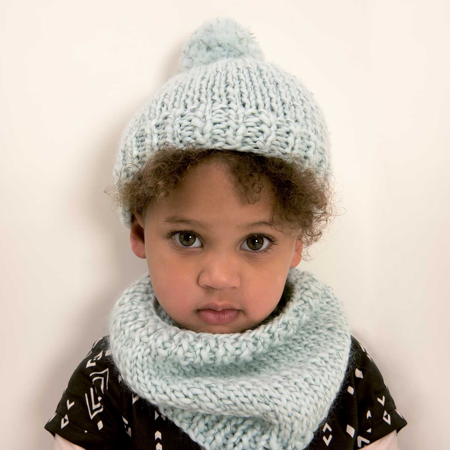 Strickanleitung Mütze und Loop aus Creative Glühwürmchen (Print). Kind trägt hellblaue Strickmütze und passenden Loop-Schal vor weißem Hintergrund.