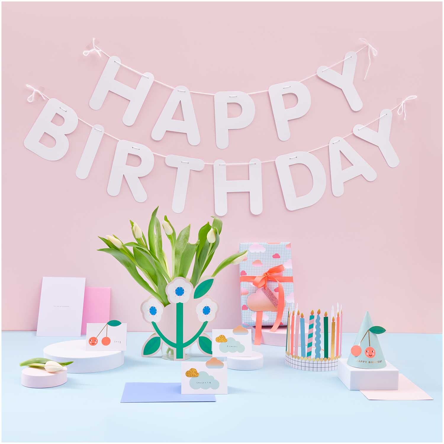 Paper Poetry Girlande Happy Birthday 5m: Weiße Buchstaben auf rosa Wand, dekoriert mit bunten Partyartikeln.