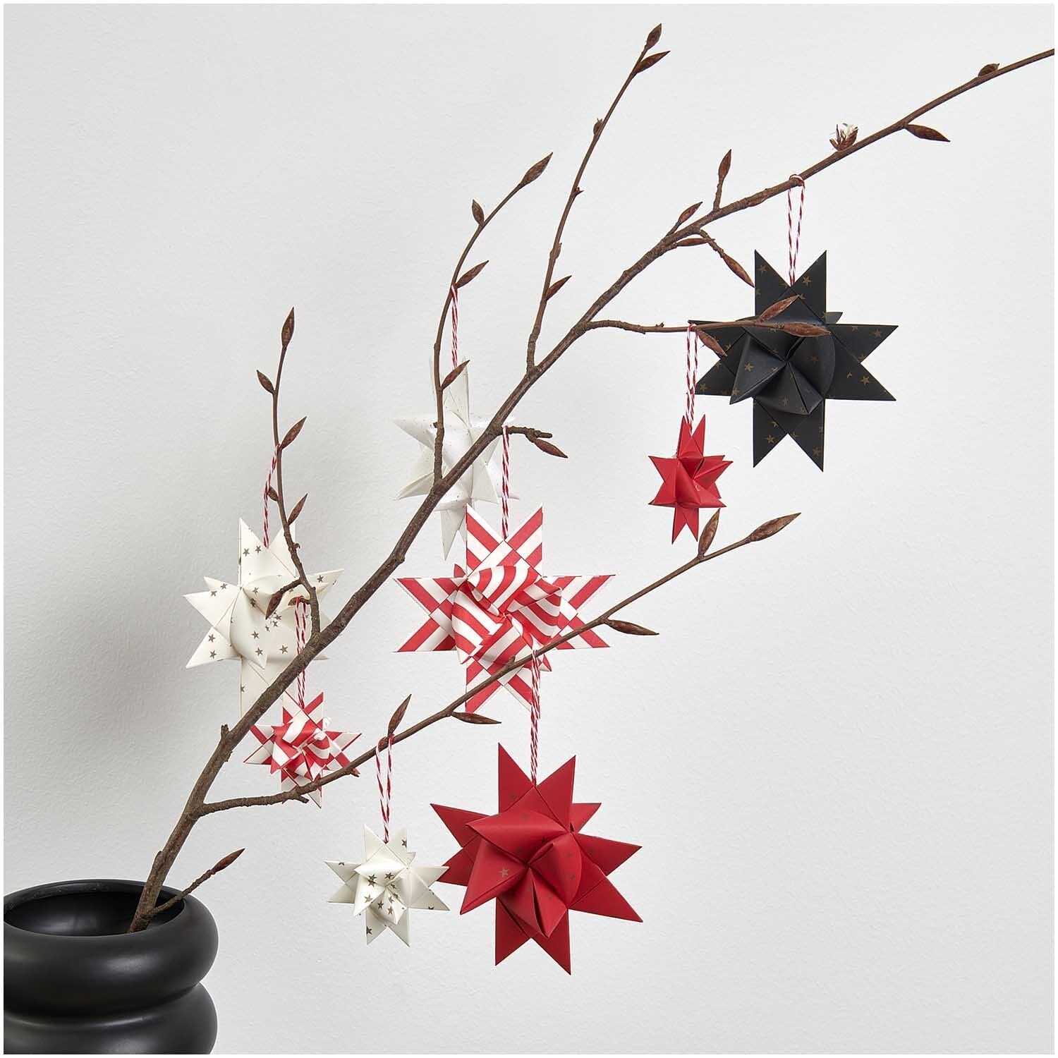 Paper Poetry Fröbelstreifen mit Recyclingpapier 60 Stück: Origami-Sterne in Rot, Weiß und Schwarz an einem Ast, dekorativ arrangiert.