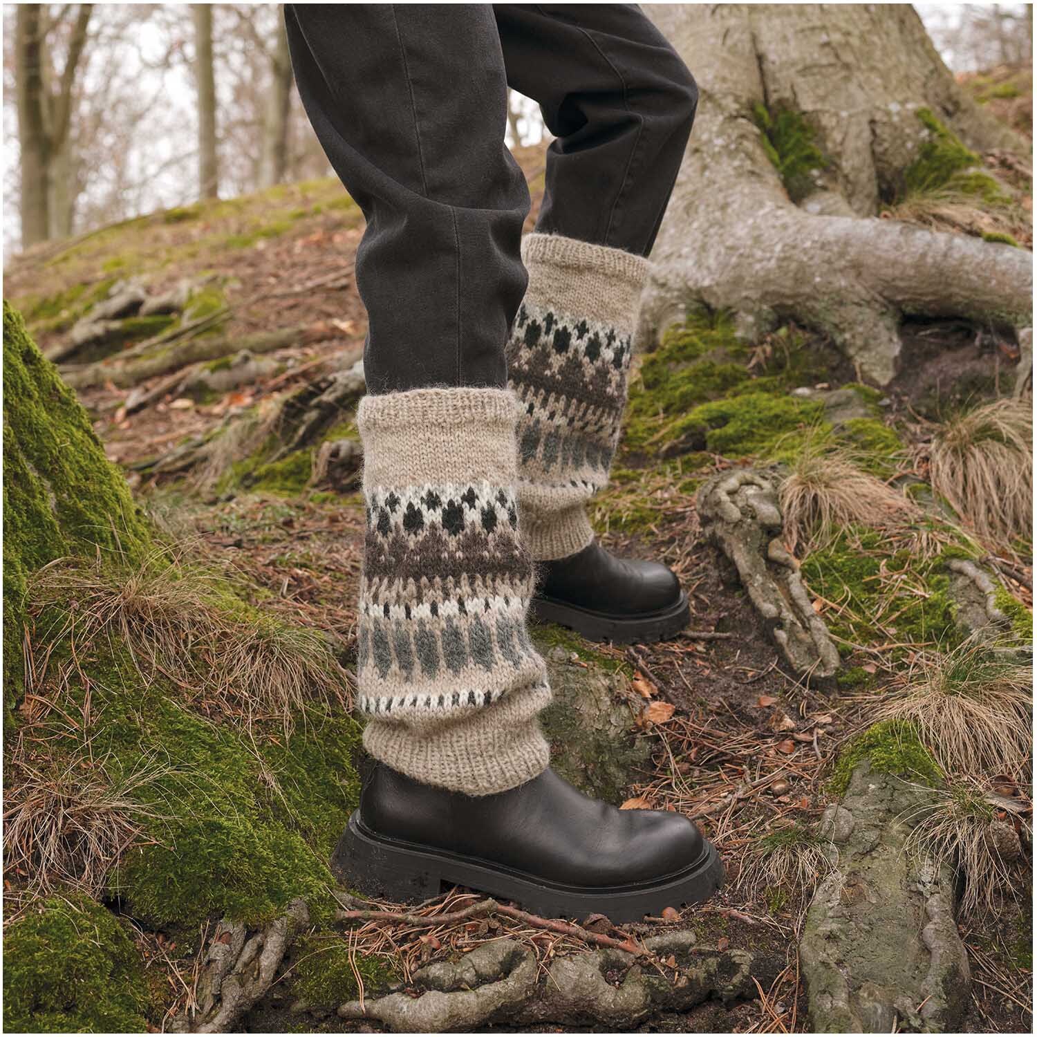 Essentials Organic Wool aran: Person trägt gestrickte Stulpen im Wald, kombiniert mit dunklen Hosen und Stiefeln.
