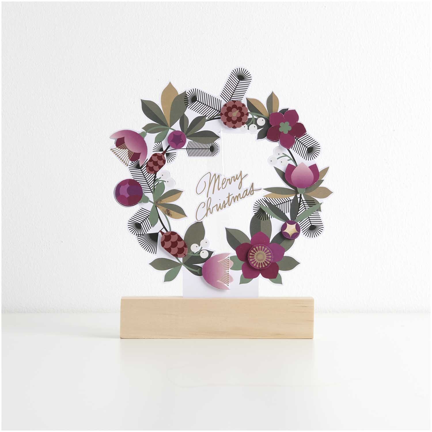 Paper Poetry Motivpapierblock Christmas Rocks! zeigt einen dekorativen Weihnachtskranz mit bunten Blumen und Blättern auf einem Holzständer.