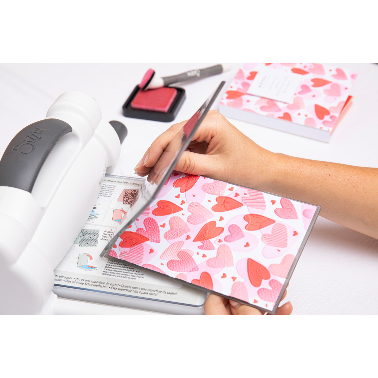 Layered Stencils Mark Making Hearts 4 Stück: Person verwendet rosa Herzschablonen mit Sizzix-Maschine.