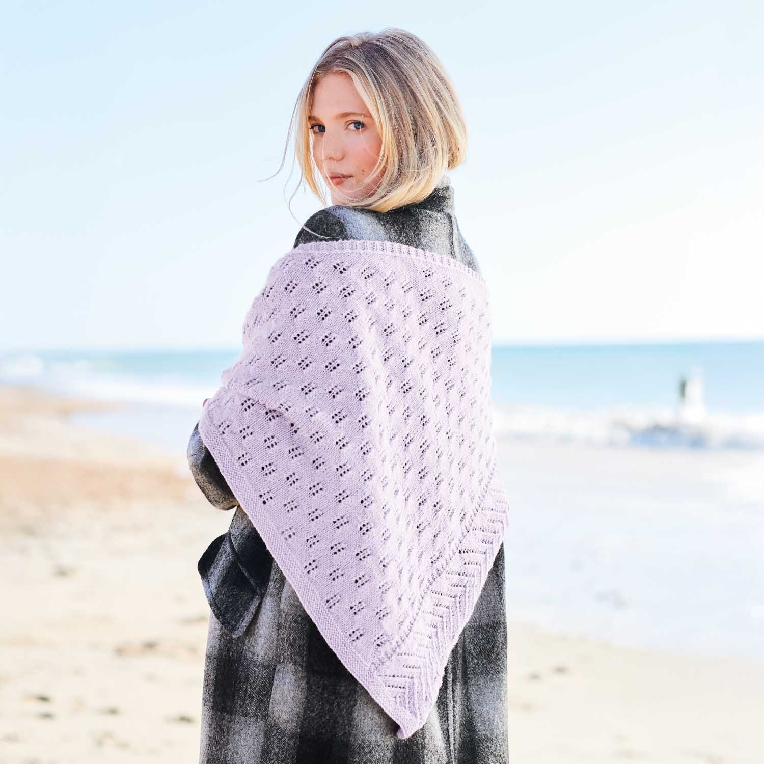 Strickanleitung Tuch aus Essentials Fine Fine Merino: Frau am Strand mit lila Tuch über Mantel.