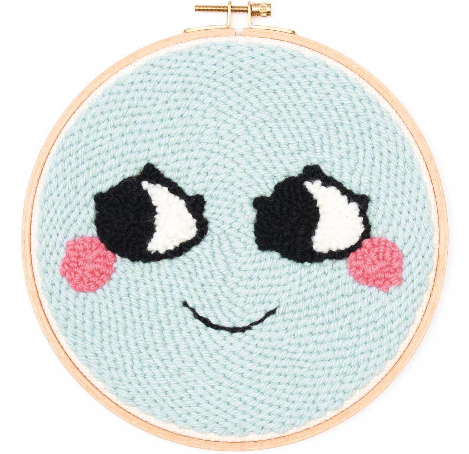Punch Needle Packung Loco Loco Gesicht mint zeigt ein lächelndes Gesicht mit großen Augen und rosa Wangen.