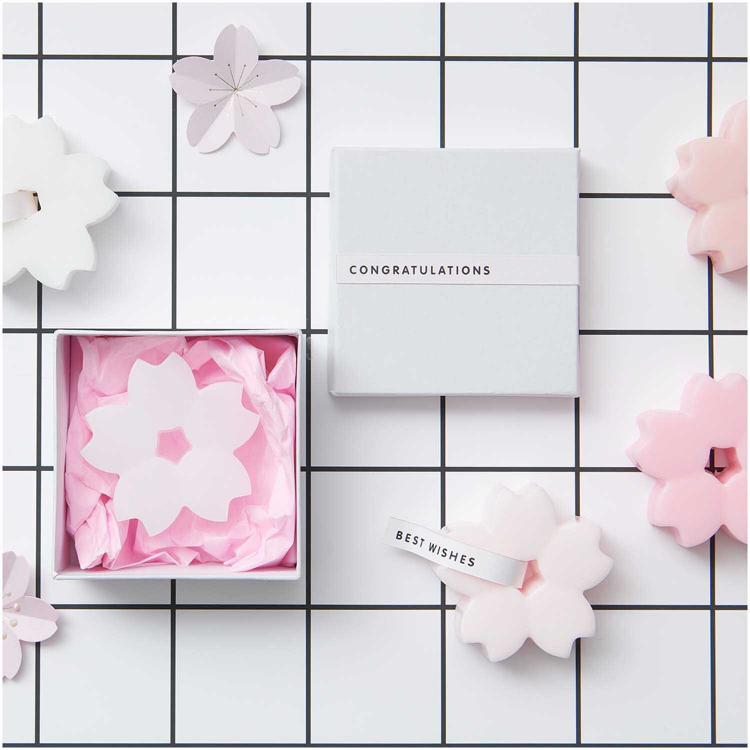Seifengießform Kirschblüten von Rico Design auf einem karierten Hintergrund mit rosa und weißen Blütenformen und Geschenkboxen.