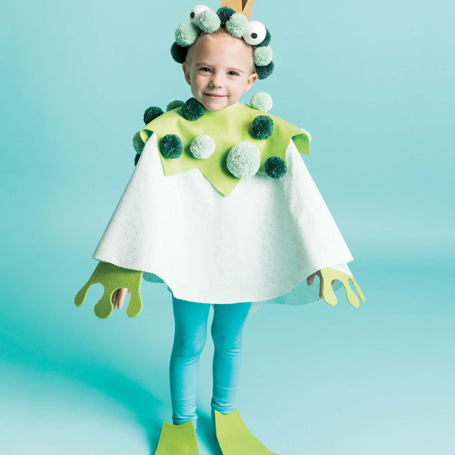 Nähanleitung Froschkostüm: Kind in grün-weißem Froschkostüm mit Pompons und Flossen auf blauem Hintergrund.