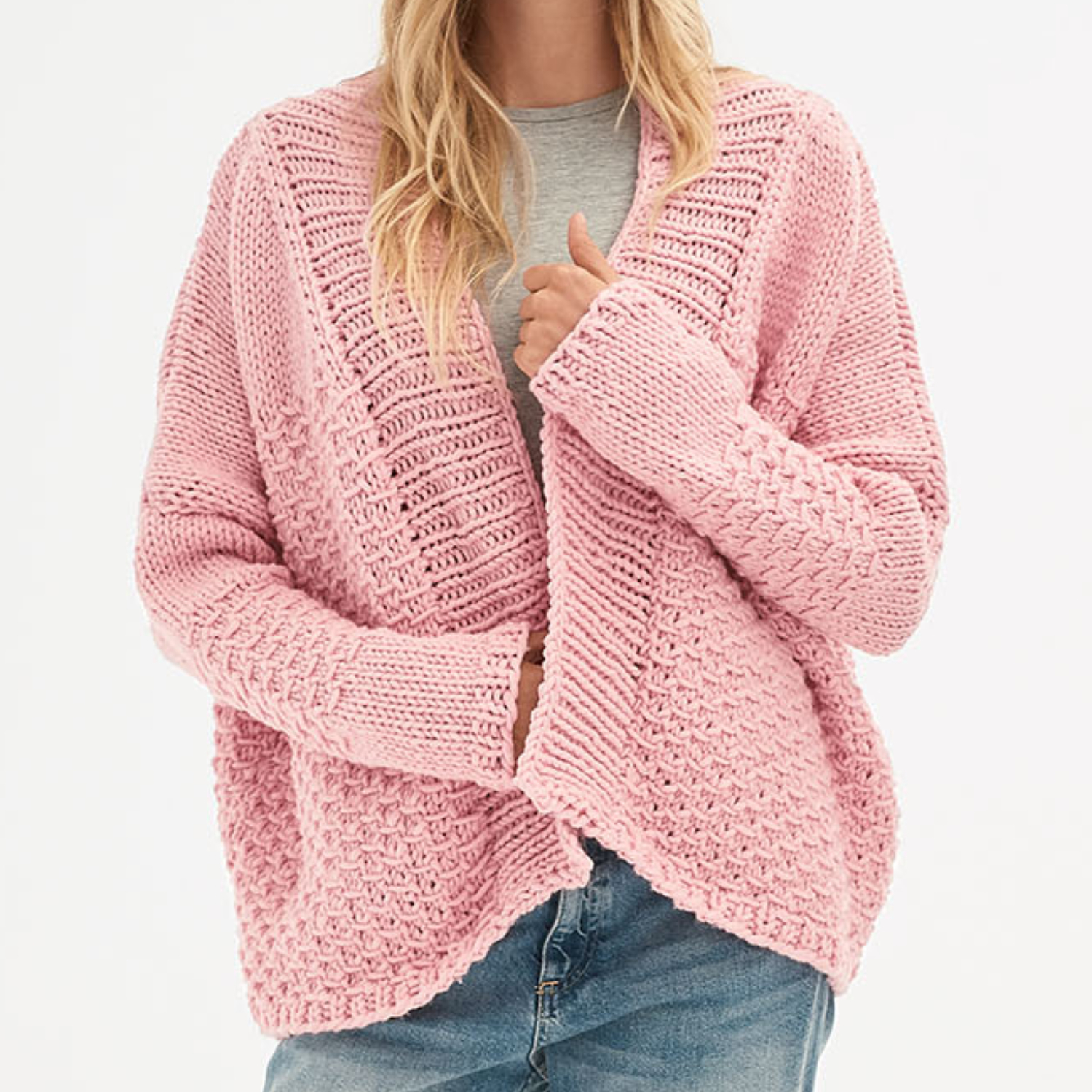 Strickanleitung Jacke aus Polar: Frau trägt eine rosa Strickjacke mit Zopfmuster über einem grauen Shirt.
