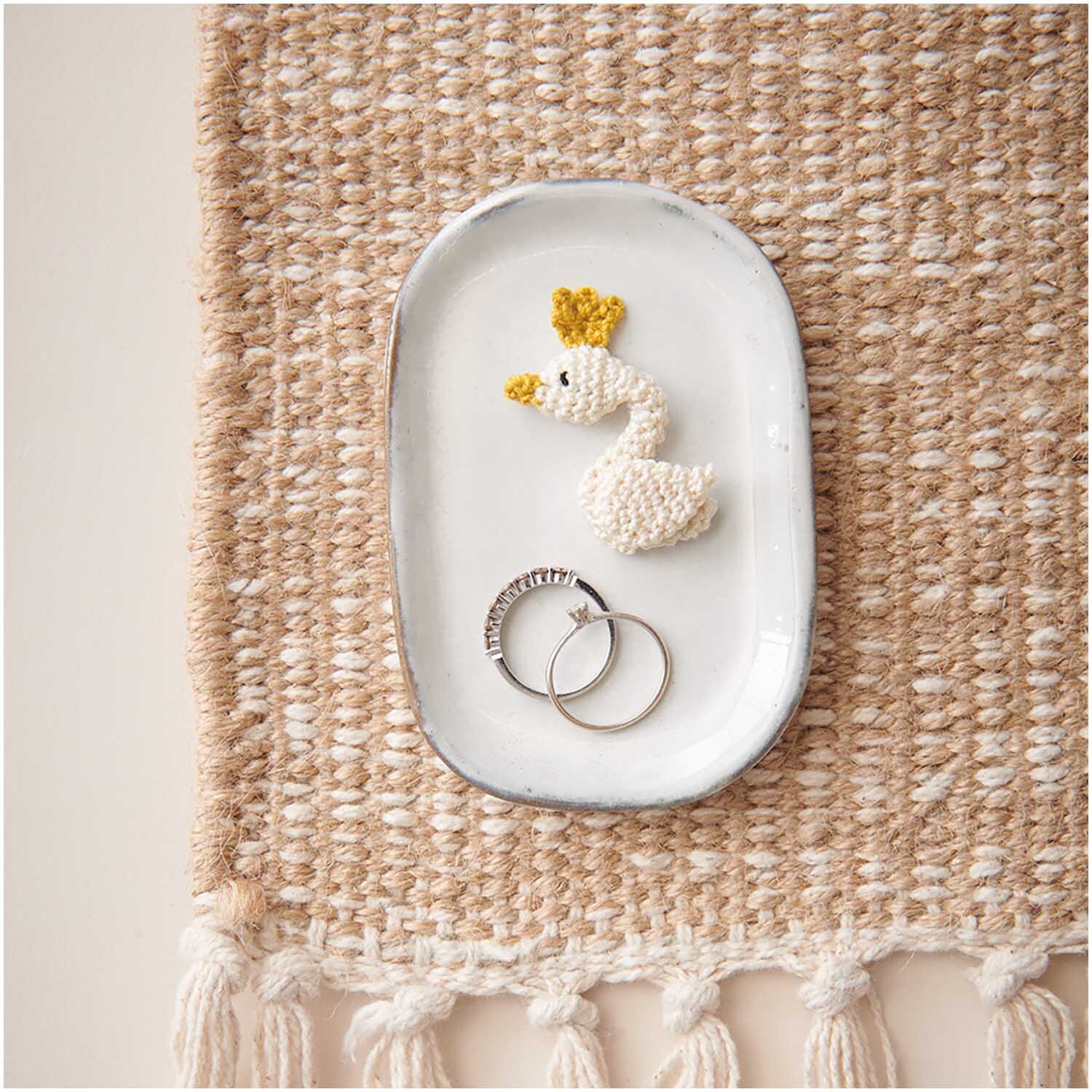 Essentials Crochet: Ein cremefarbenes Häkelgarn von Rico Design, präsentiert auf einem Tablett mit Schmuck.