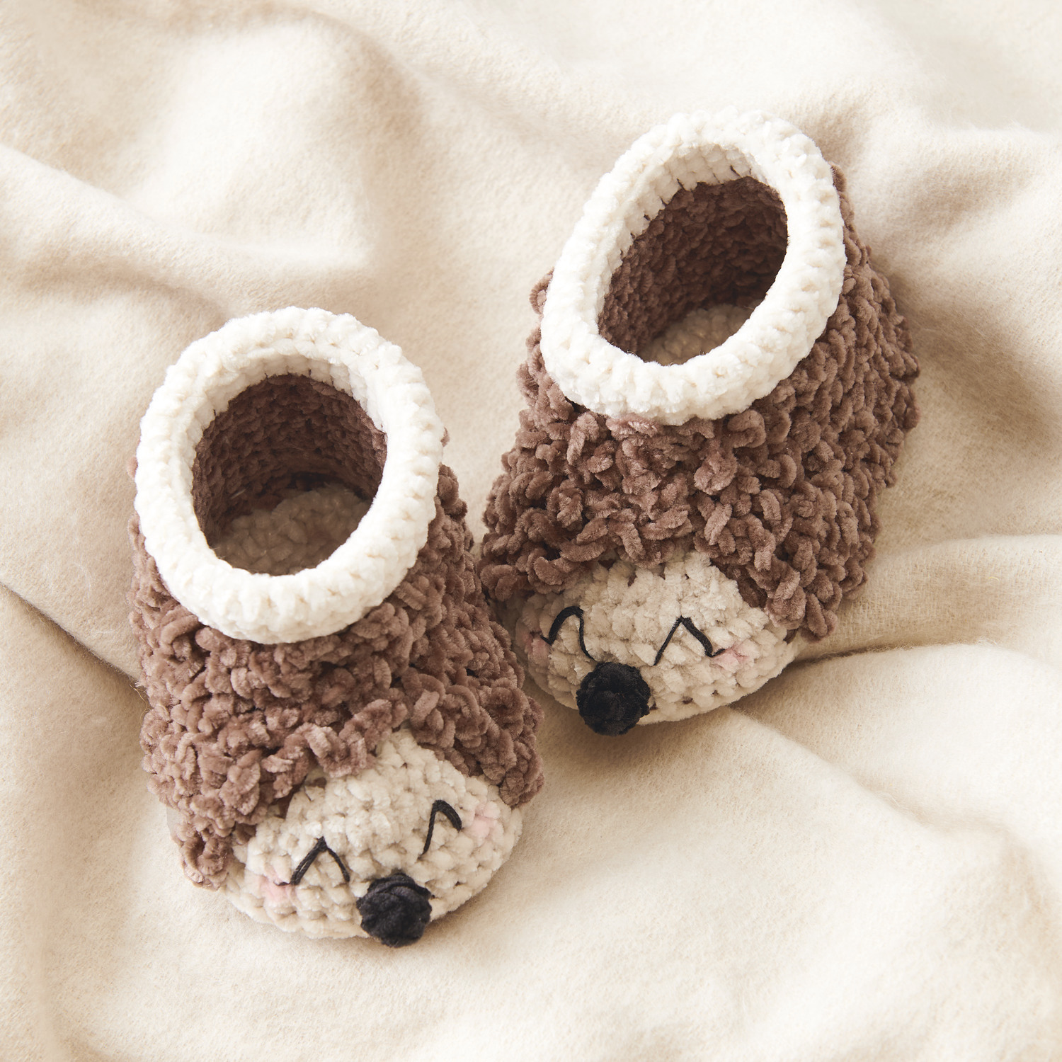 Ricorumi Nilli Nilli Häkelset Baby Booties Igel in Creme und Schokolade auf beigem Stoff. Ideal für DIY-Projekte und kreative Geschenke.