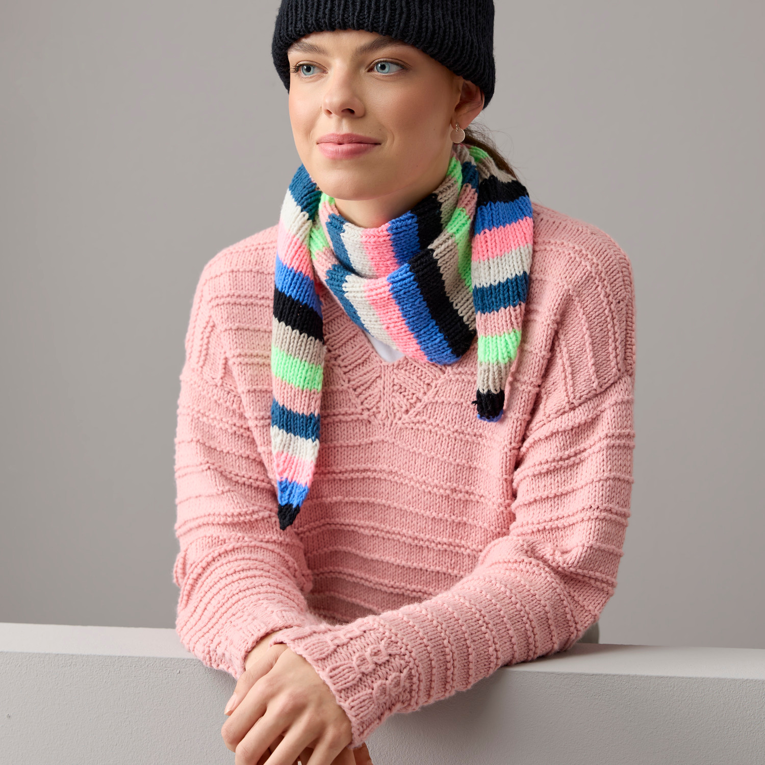 Strickset Dreieckstuch Modell 05b aus Vegan Cashmere: Frau trägt gestreiften Schal in Blau, Grün, Pink und Schwarz, kombiniert mit altrosa Pullover.