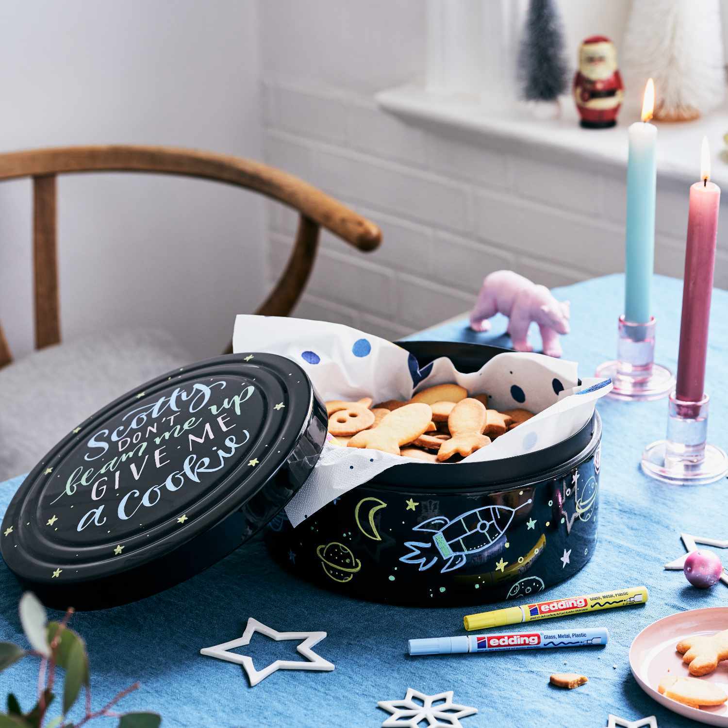751 Glanzmarker auf einem Tisch mit Keksen in einer dekorativen Dose, umgeben von Kerzen und Weihnachtsdekoration.