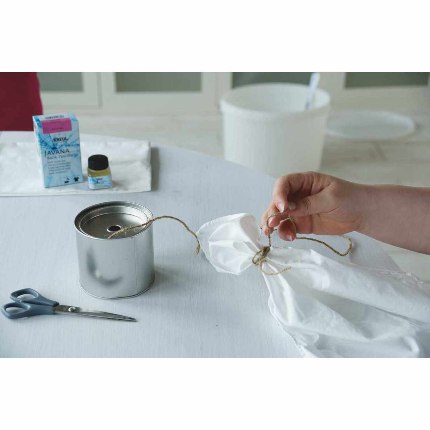 Javana Batik-Textilfarbe: Hand knotet Stoff neben Dose und Schere, KREUL-Produkt im Hintergrund.