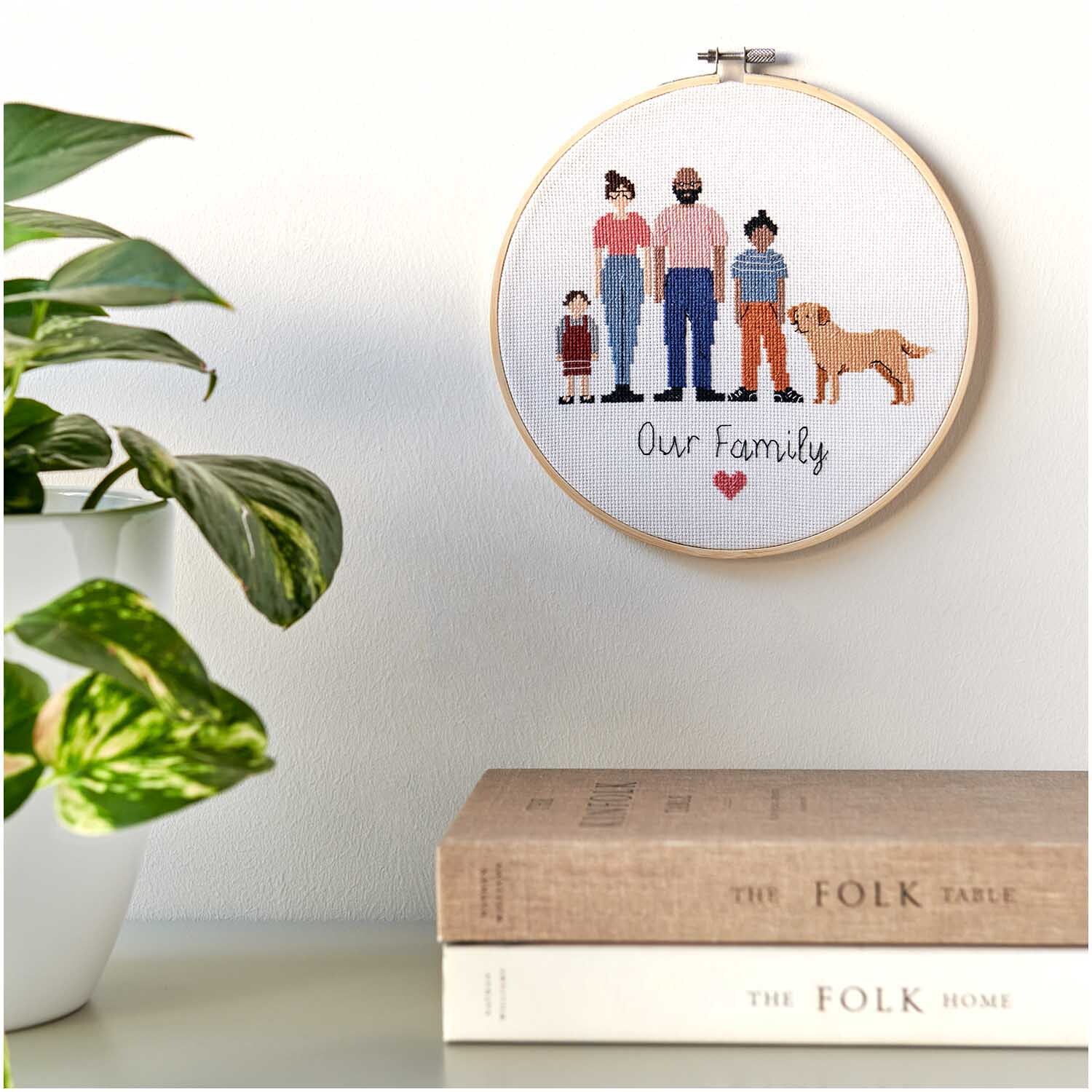 Figurico Stickpackung Family 20cm zeigt eine gestickte Familie mit Hund in einem Holzrahmen.