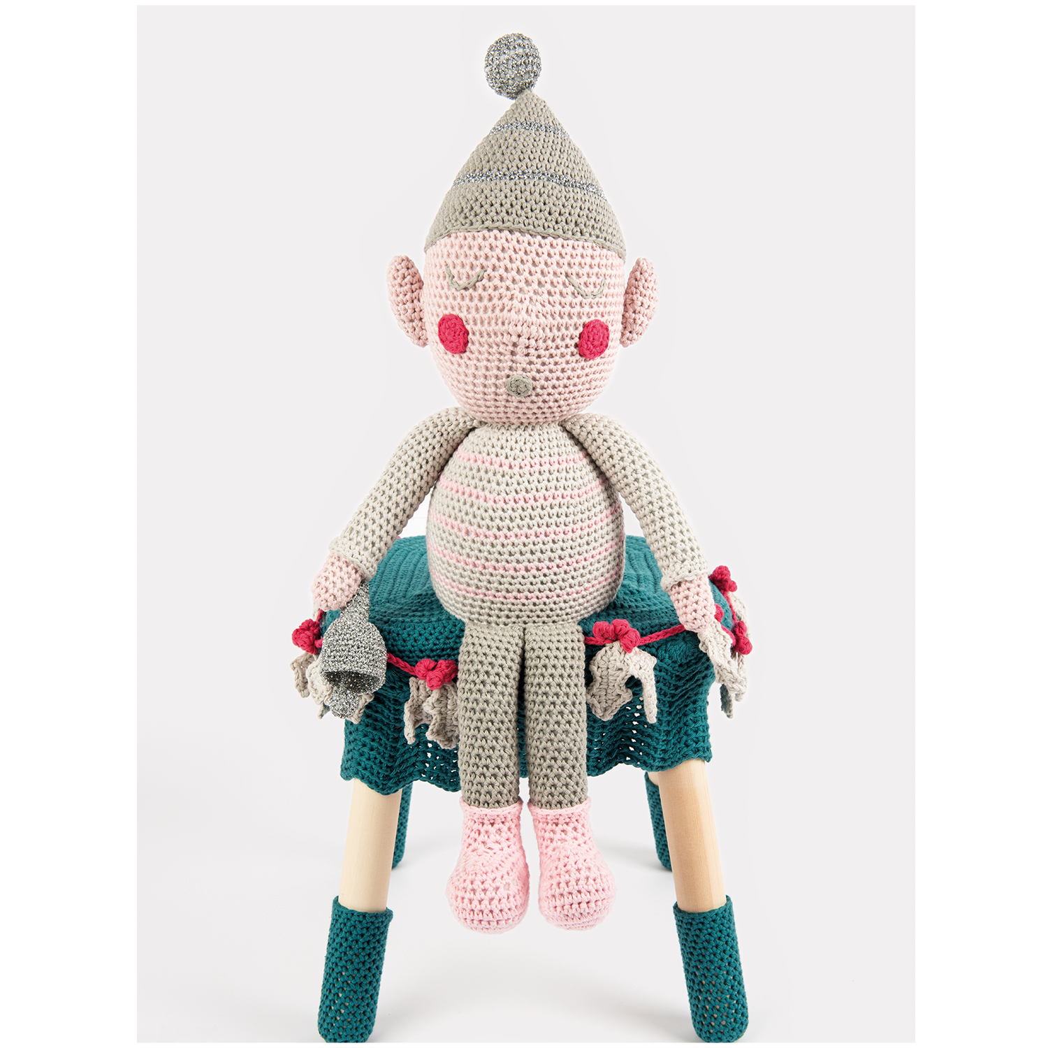 Creative Cotton aran: Gehäkelte Puppe mit Mütze sitzt auf einem dekorierten Hocker, umgeben von bunten Garnen.