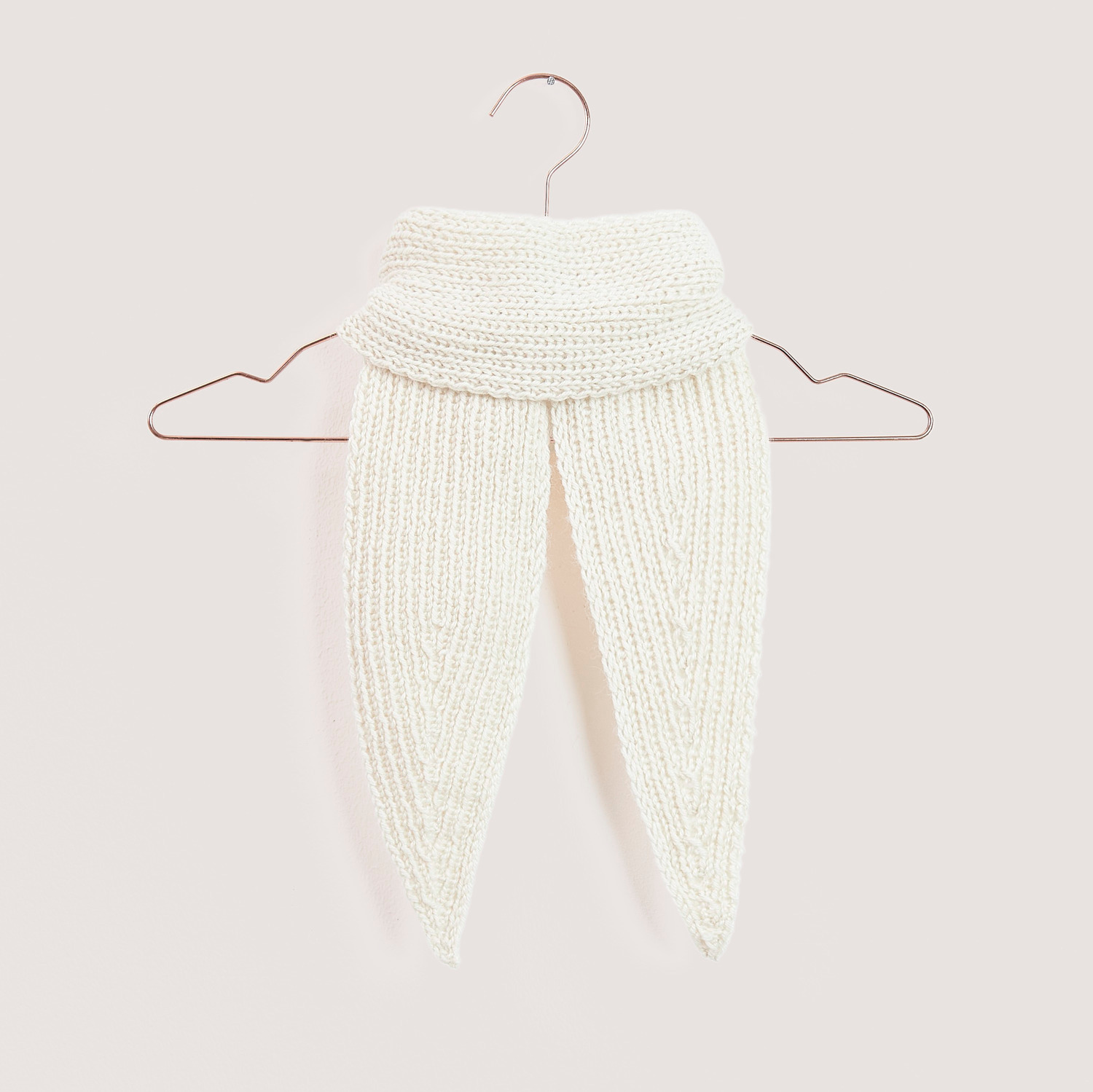 Strickset Mini Tuch Modell 04a: Ein cremefarbenes, gestricktes Tuch von Rico Design auf einem Kleiderbügel.