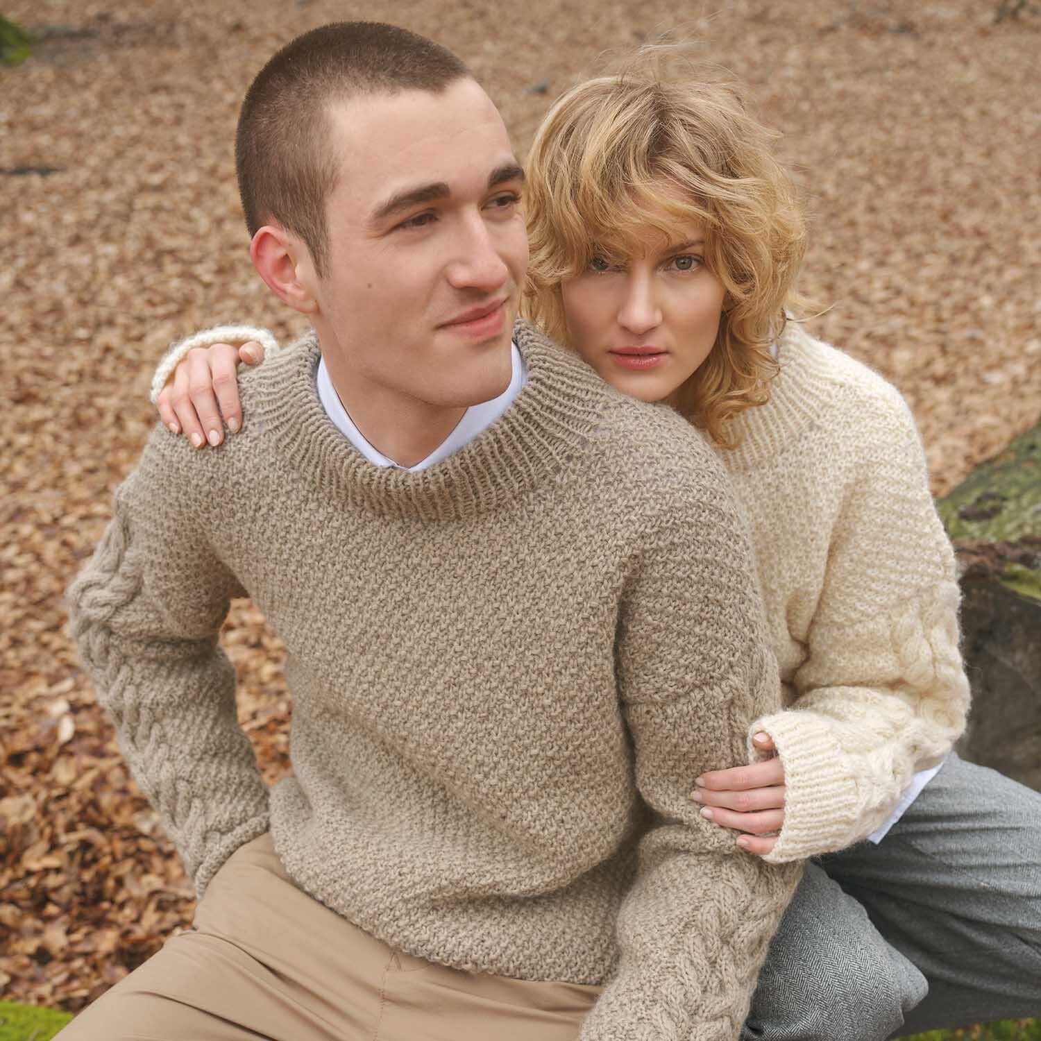 Strickanleitung Pullover aus Essentials Organic Wool aran: Zwei Personen in gestrickten Pullovern sitzen auf einem Baumstamm im Herbstwald.