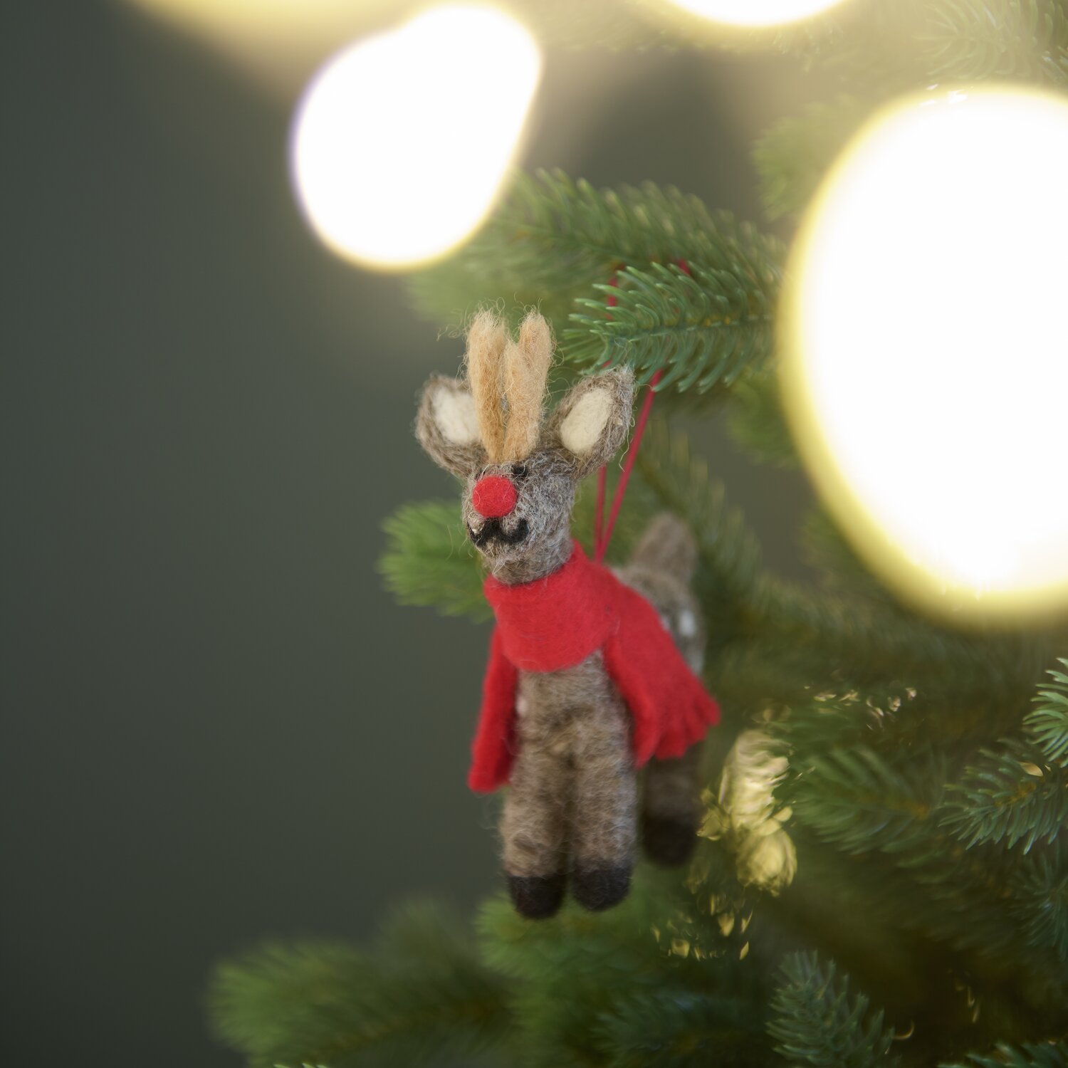 Aufhänger Filz-Hirsch mit Schal: Brauner Hirsch aus Filz mit rotem Schal, hängend an einem Weihnachtsbaum. Größe 12x8x2,5cm.