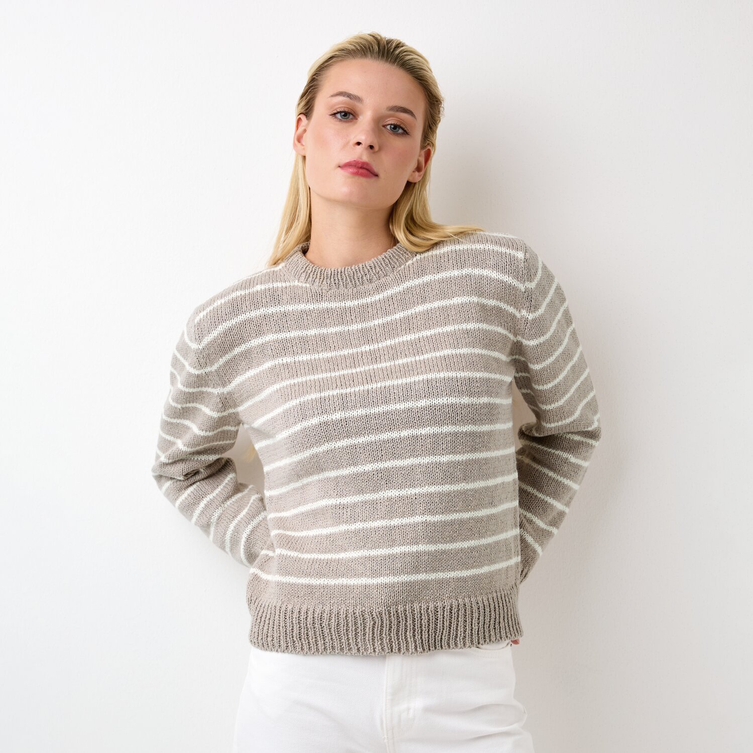 Strickset Pullover Modell 06 aus Die Neue Masche No. 12, beige-weiß gestreift, lässig geschnitten, präsentiert von einer Frau vor weißem Hintergrund.
