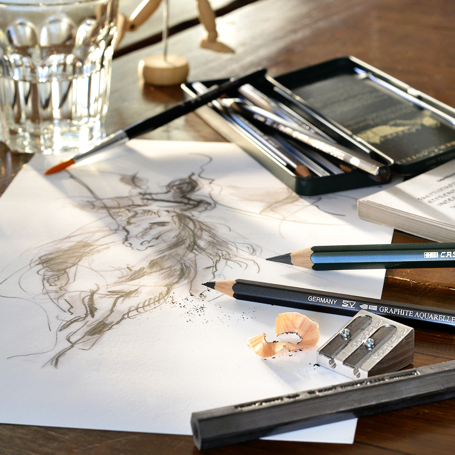 Graphite Aquarelle Künstlerbleistift, Faber Castell, 5 Stück im Metalletui, auf einem Tisch mit Skizze und Spitzer. Ideal für detailreiche Zeichnungen.