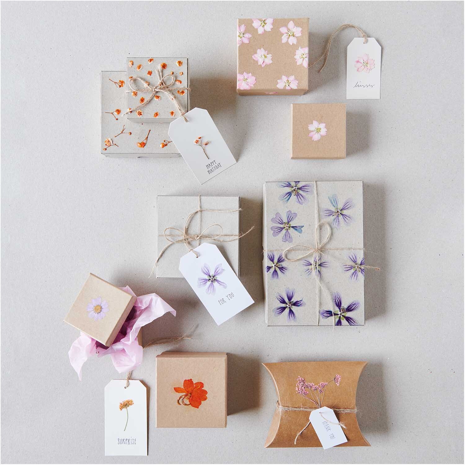 Gepresste Blüten Schleierkraut orange 8 Stück auf Geschenkboxen, dekoriert mit floralen Mustern und Anhängern. Ideal für kreative Verpackungen.