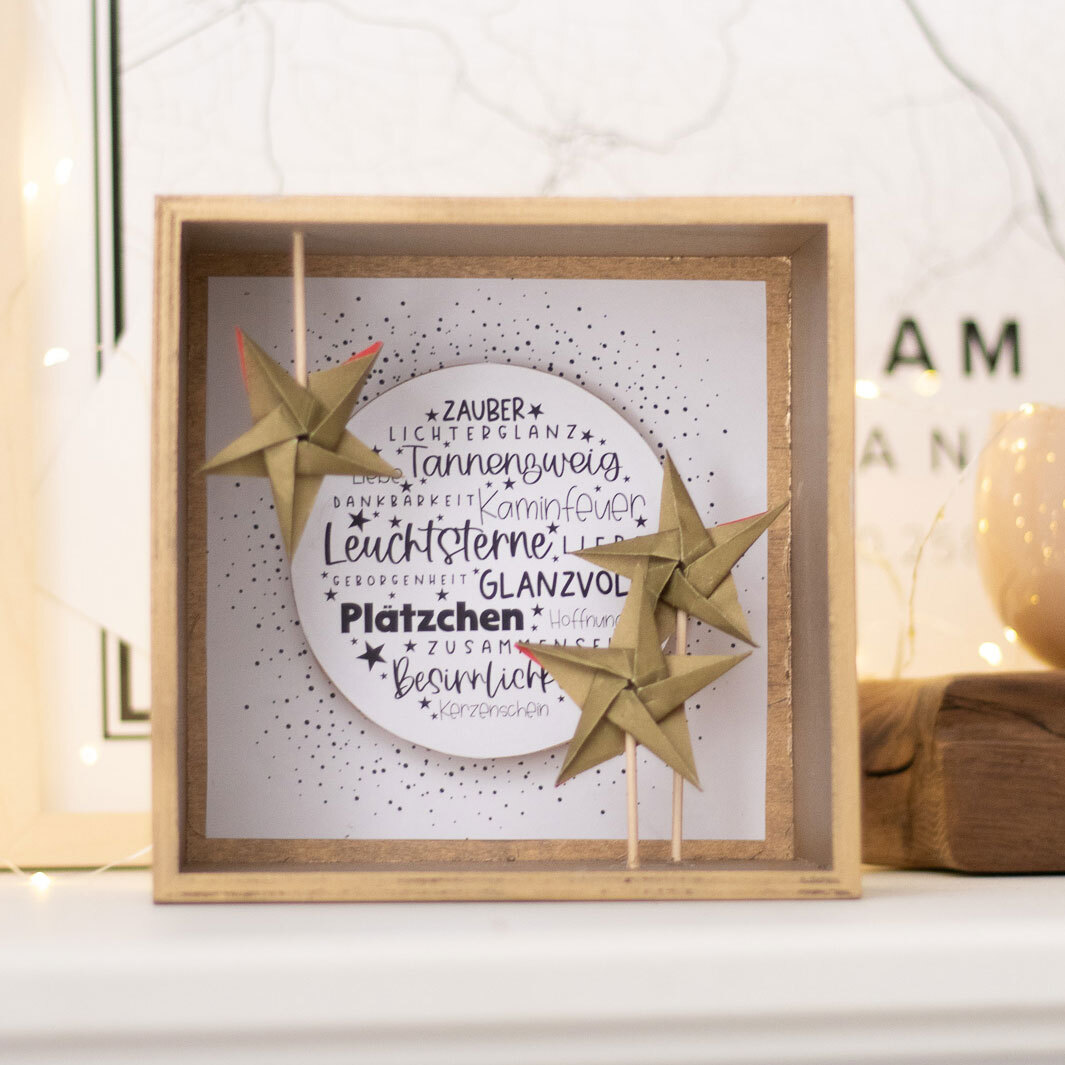 Inspiration 3D-Sternendeko: Dekoratives Holzdisplay mit goldenen Sternen und festlichen Schriftzügen.
